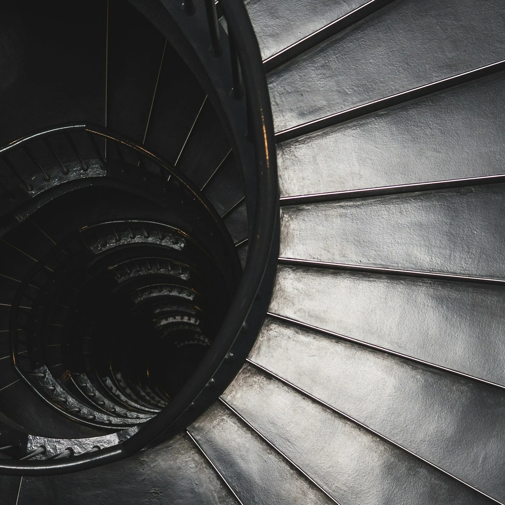 Top view of a spiral staircase with black steps and railings, viewed from above.