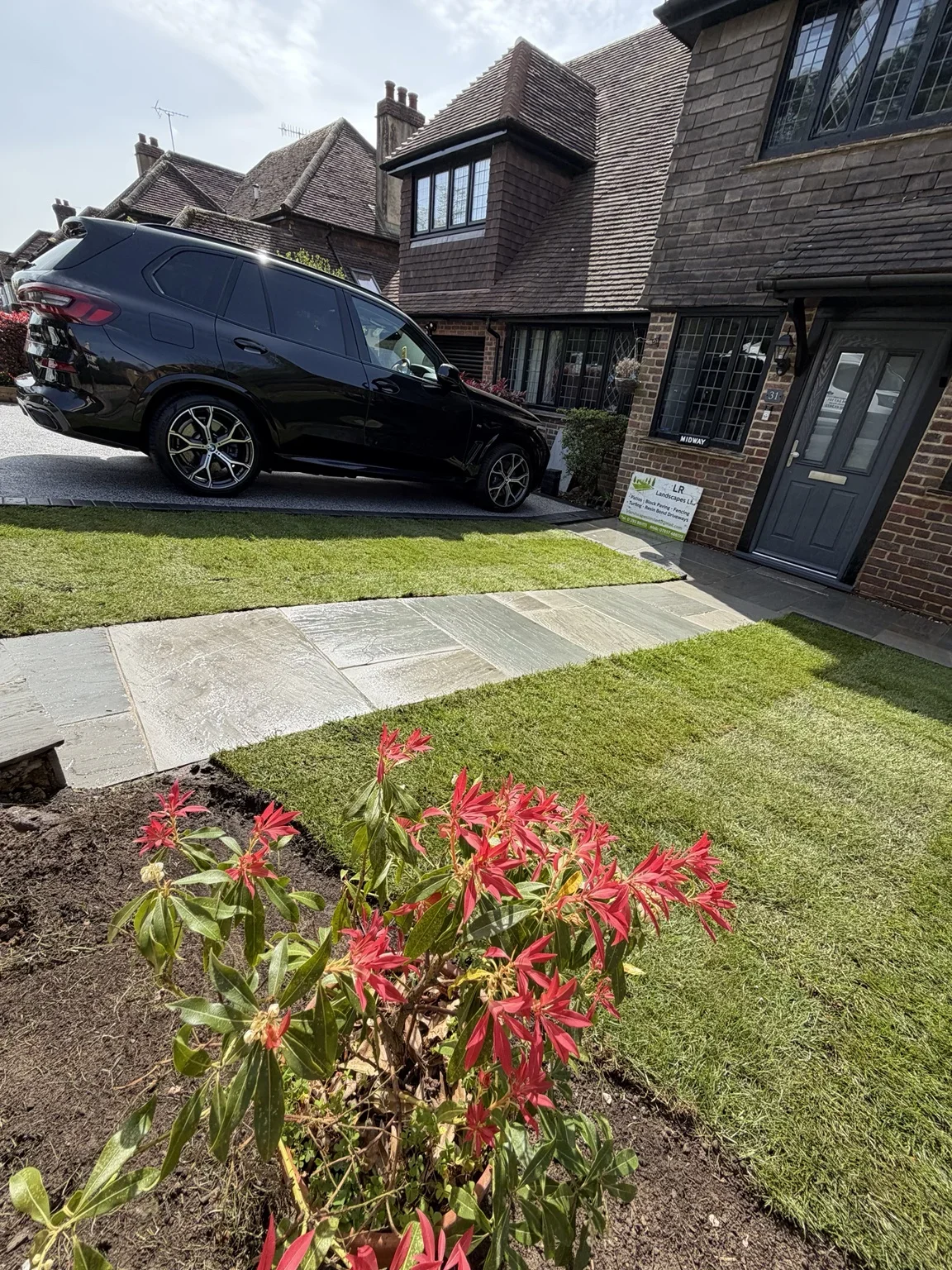 Driveway and front garden — the resin bound parking area meets a curved lawn edge, with planted borders adding colour beside the entrance.