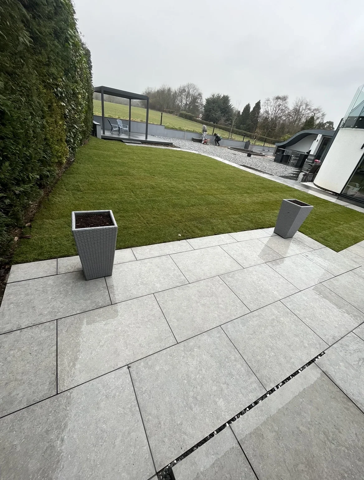 Patio and lawn connection — pale grey paving frames a rectangular lawn, with steps and planters defining the change in level.
