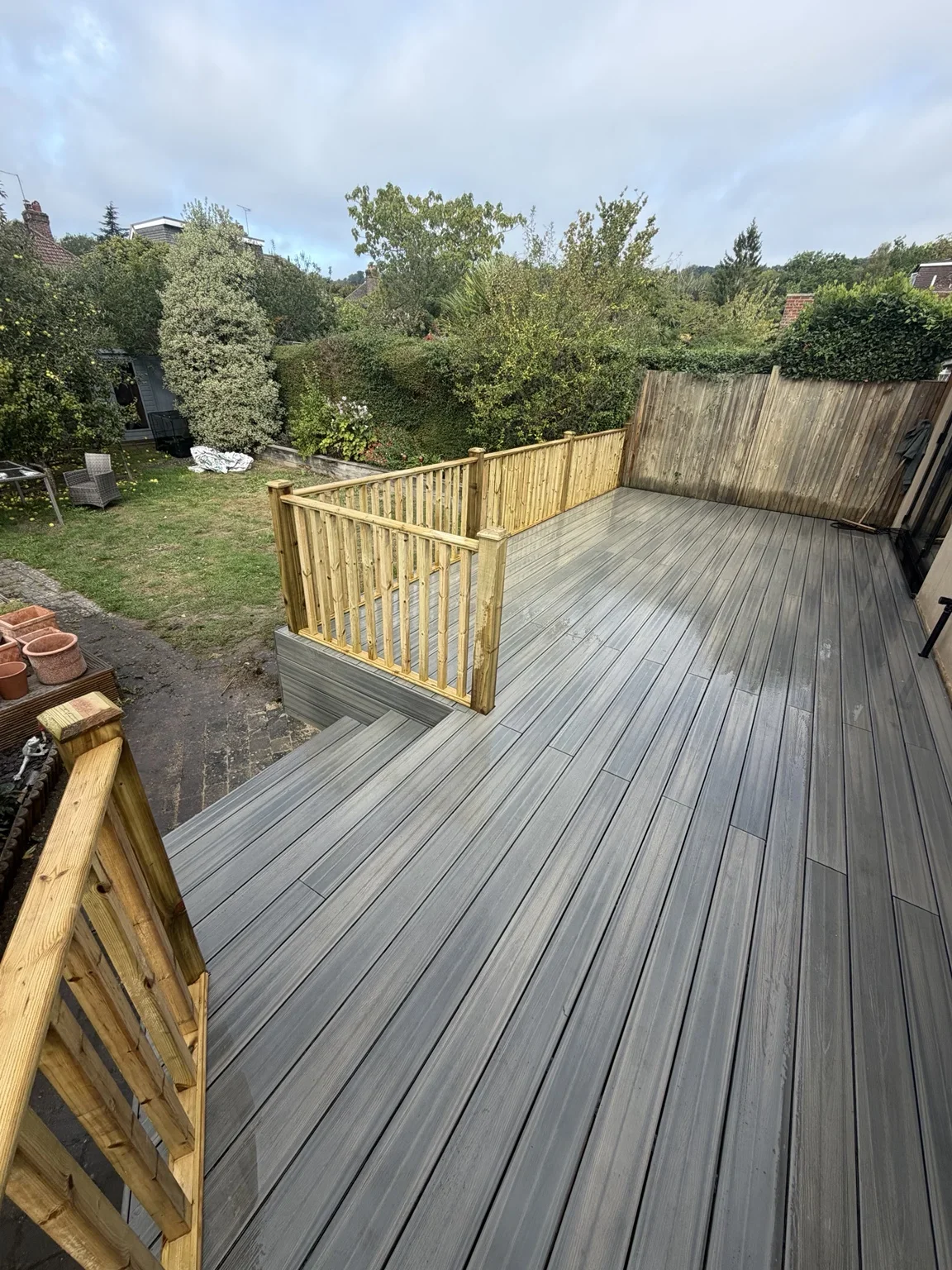 Composite decking — grey boards form a raised seating area, with timber balustrades and steps connecting the deck to the garden.