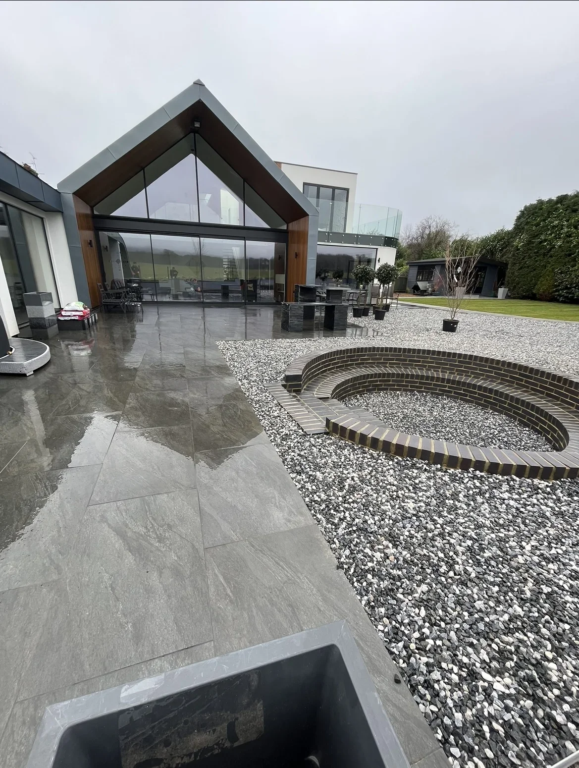 Garden transformation — grey paving links the glazed garden building to gravel beds, with a circular feature forming the centre of the outdoor space.