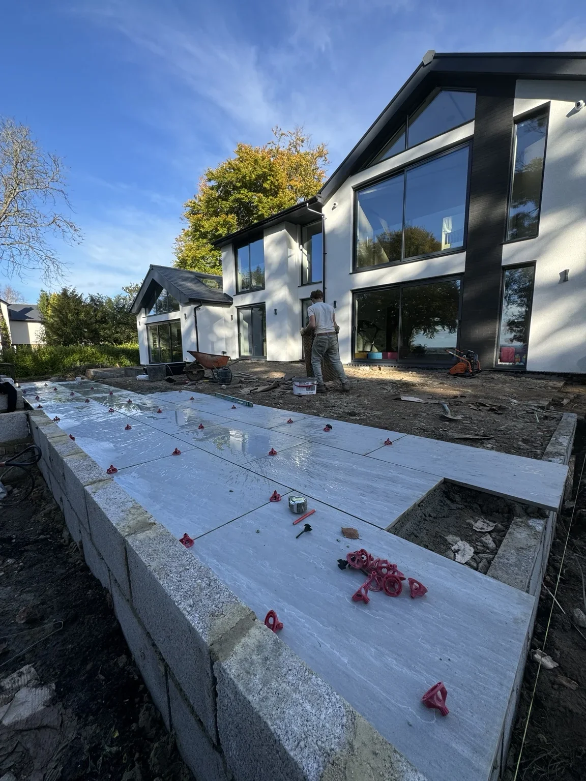 Porcelain patio in progress — tiles are being laid beside the house, with the terrace edge and broad steps taking shape during installation.