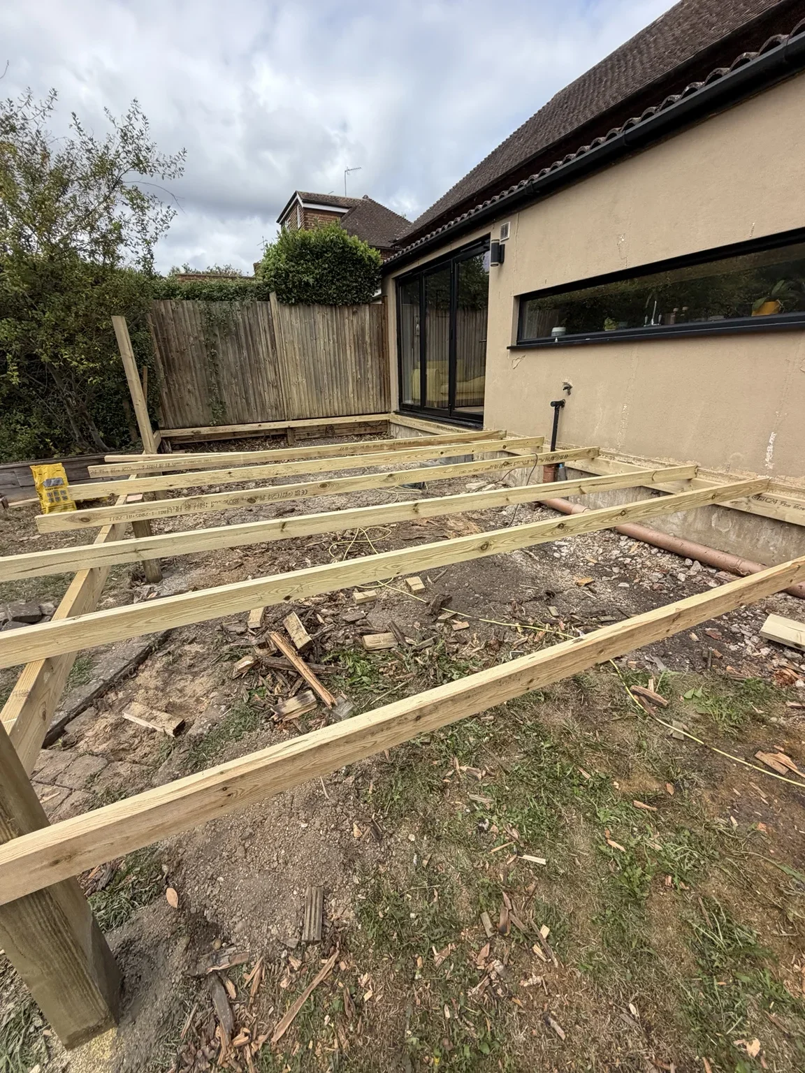 Decking framework in progress — timber joists form the supporting structure beside the house before the composite boards are fitted.