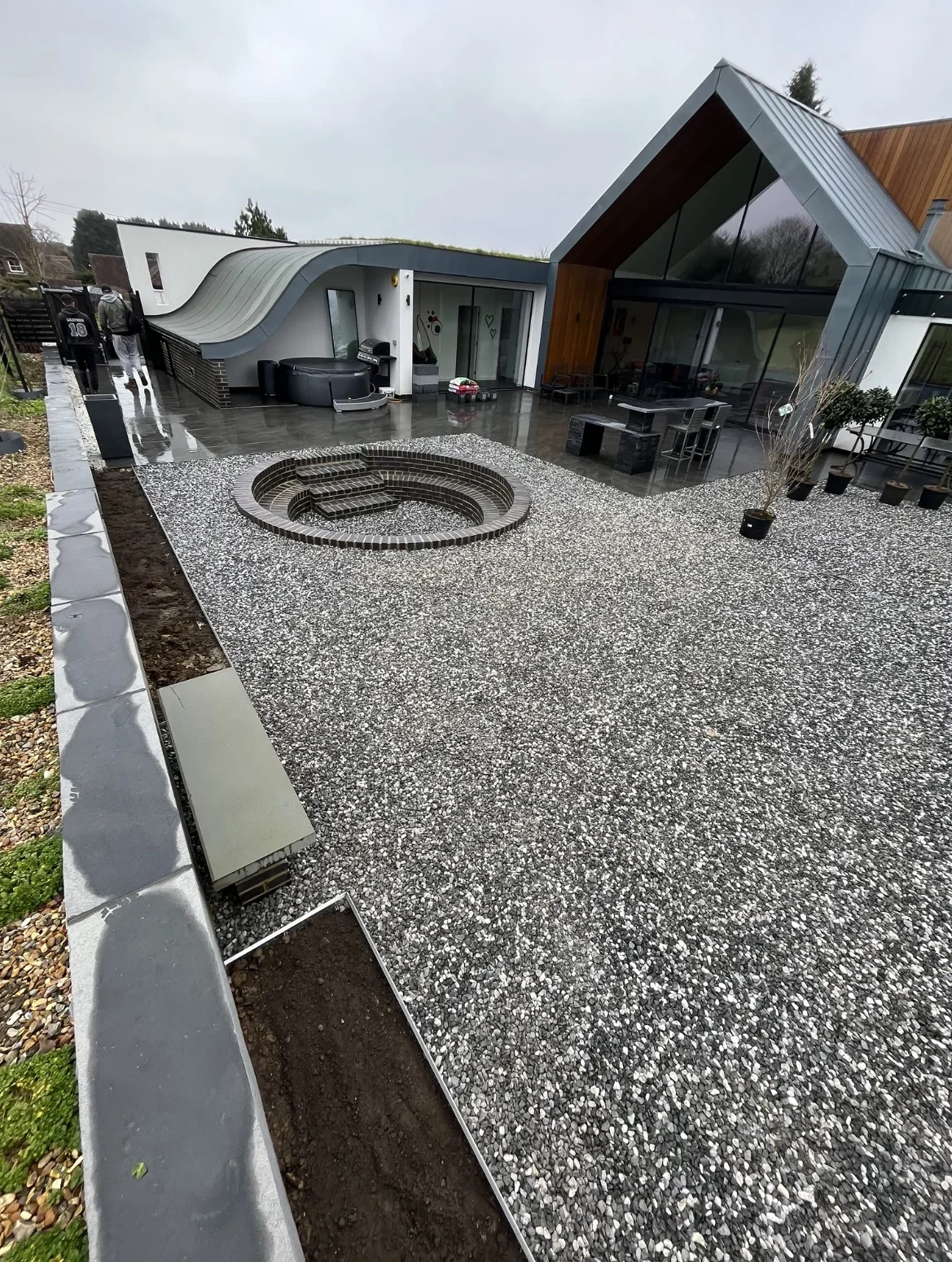 Garden paving detail — raised grey-edged borders surround gravel beds and a circular feature, beside the glazed garden building.