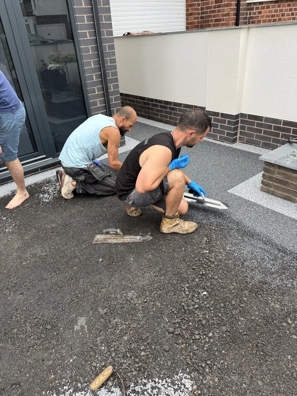 Resin bound installation in progress — the surface is being spread and hand-trowelled beside the entrance steps, working carefully around the edging.