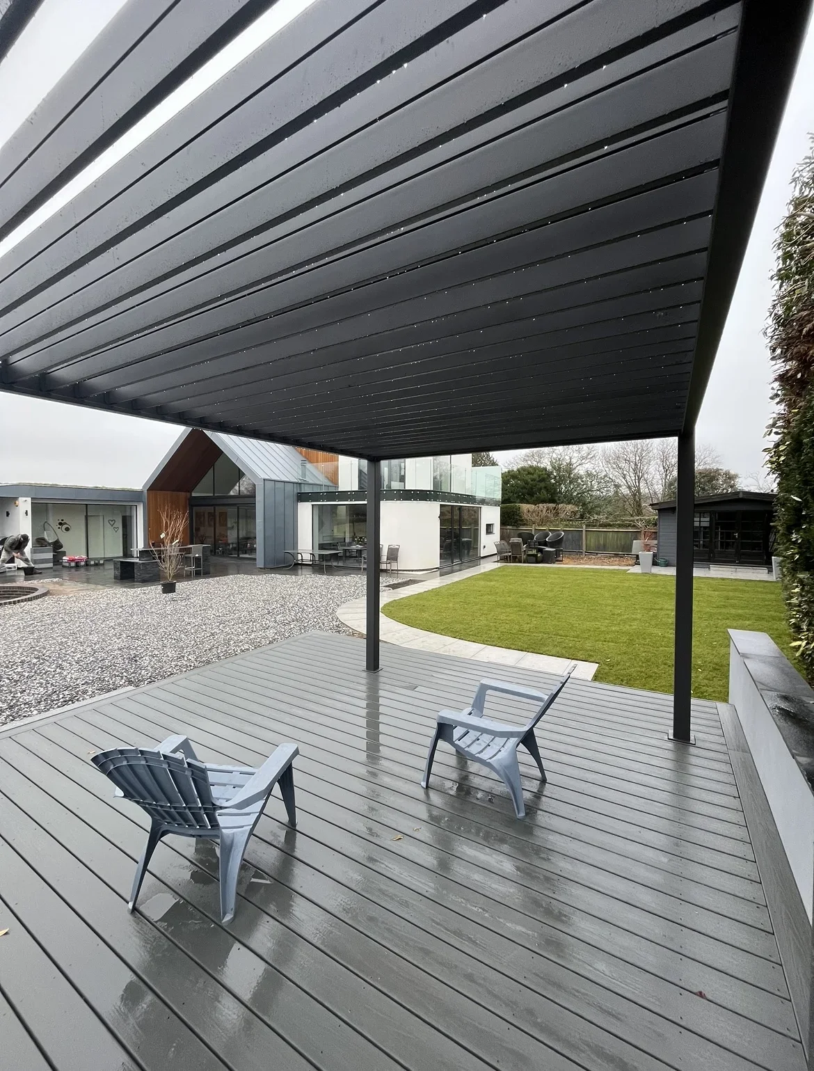 Sheltered garden decking — a grey deck creates space for outdoor seating beneath a slatted canopy, overlooking the lawn and paved terrace.