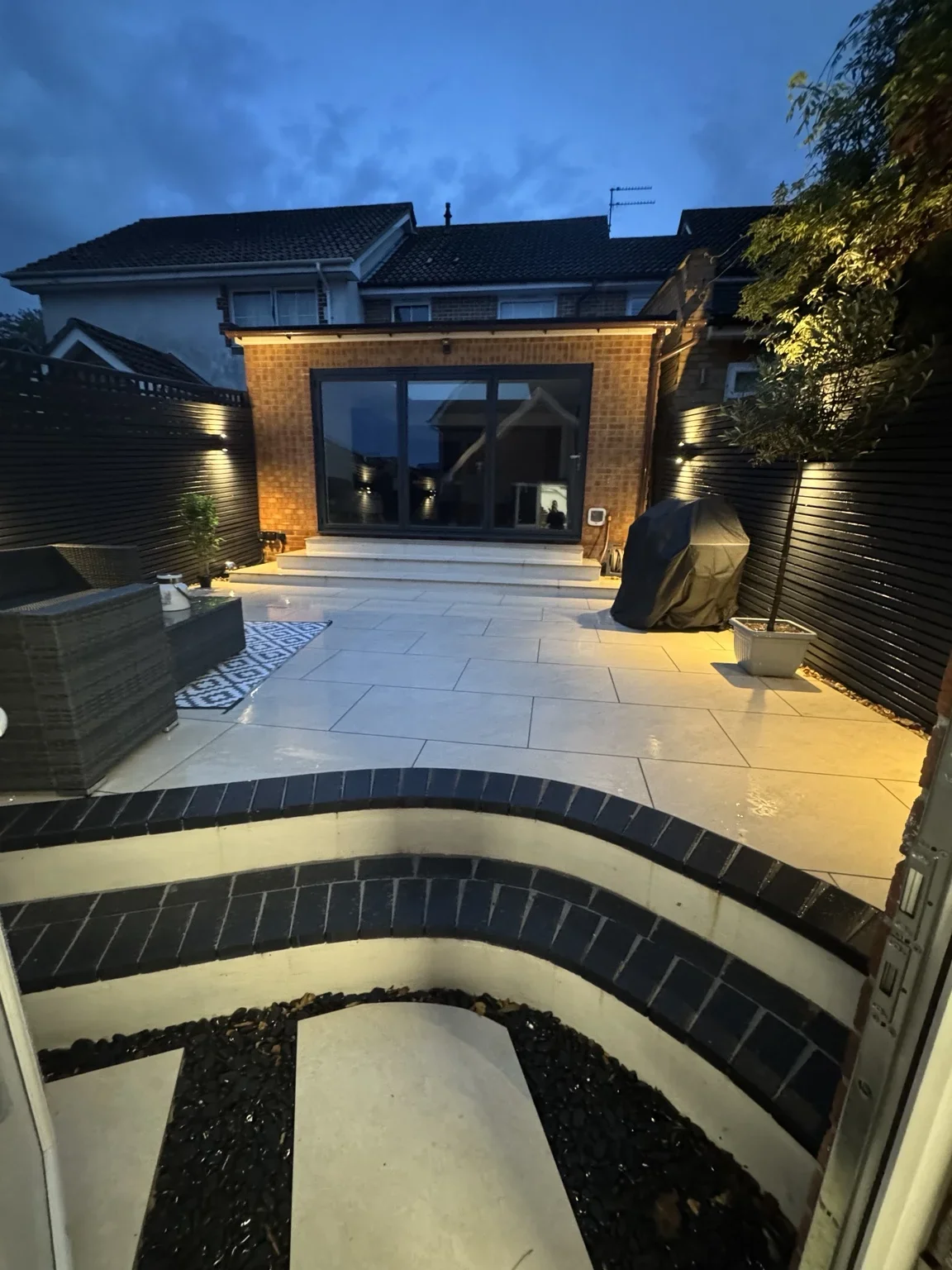 Curved steps at night — illuminated stone treads lead up to the patio, with curved brick risers forming a distinct entrance to the seating area.