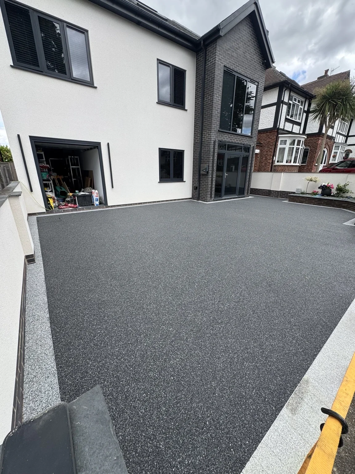Resin bound driveway — a close view of the finished surface beside the white house, framed by pale edging and the boundary fence.