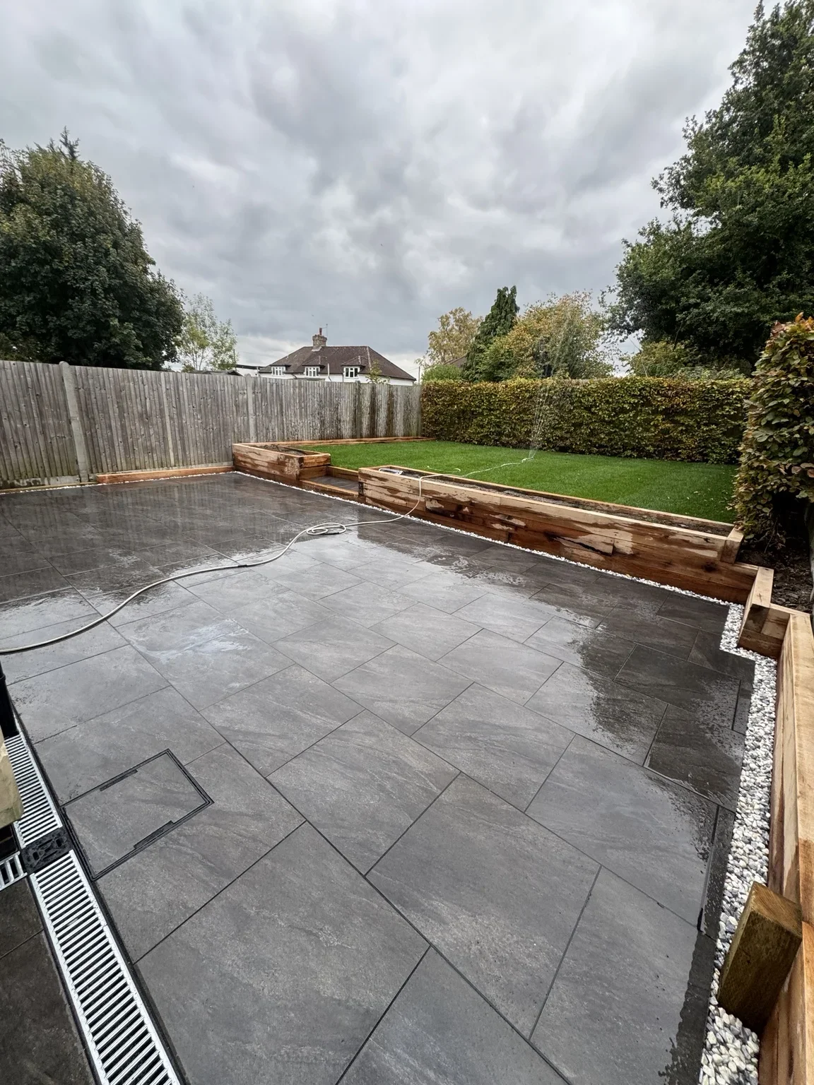 Garden patio — grey rectangular paving creates a terrace alongside the lawn, with raised brick borders defining the garden edge.