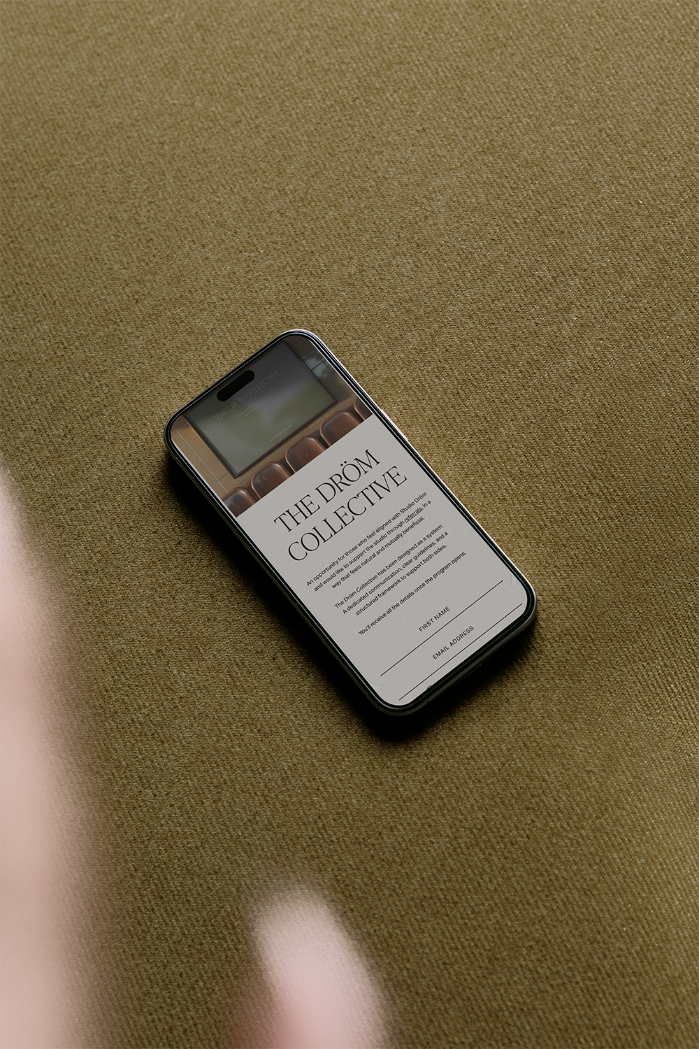 Le smartphone affiche le site web « The Drom Collective » sur une surface en tissu beige.