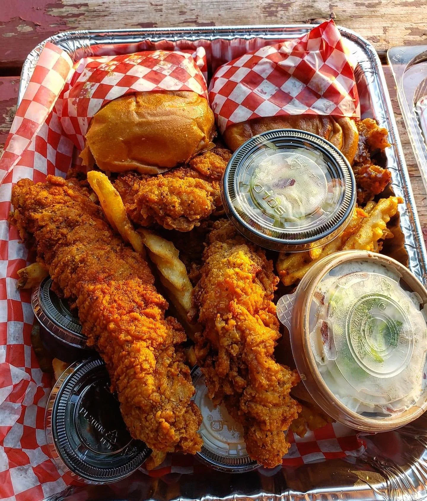Tray of fried chicken tenders, fried fish fillets, sandwich buns, French fries, small containers of dipping sauce, and a salad in a plastic cup.