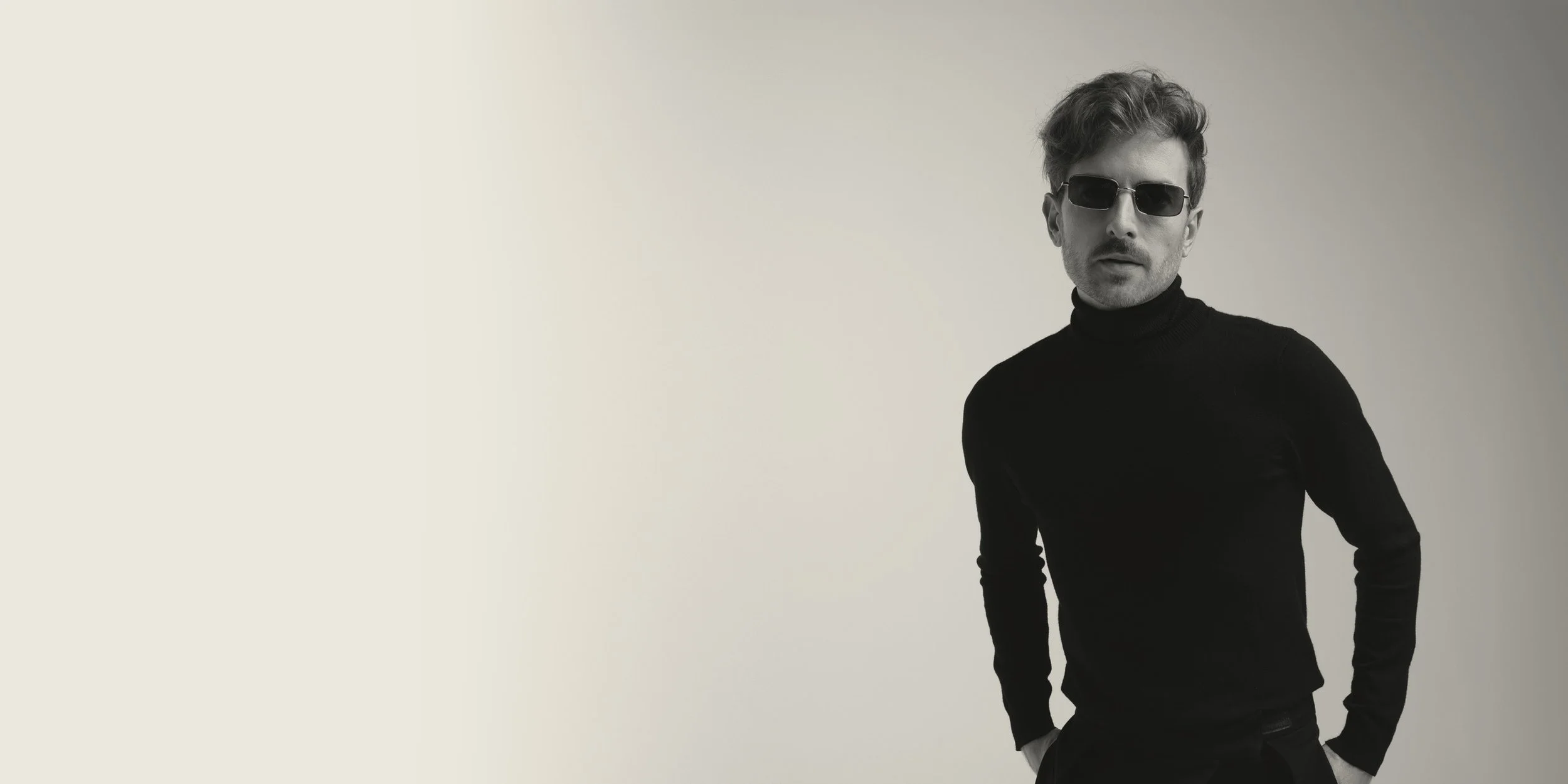 Black-and-white photo of Evan Nathaniel Grim wearing dark sunglasses and a black turtleneck sweater, standing against a plain background.