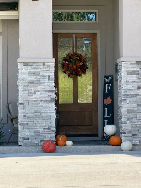 Decorated front porch with fall pumpkins, a wreath, and a 'Happy Fall' sign