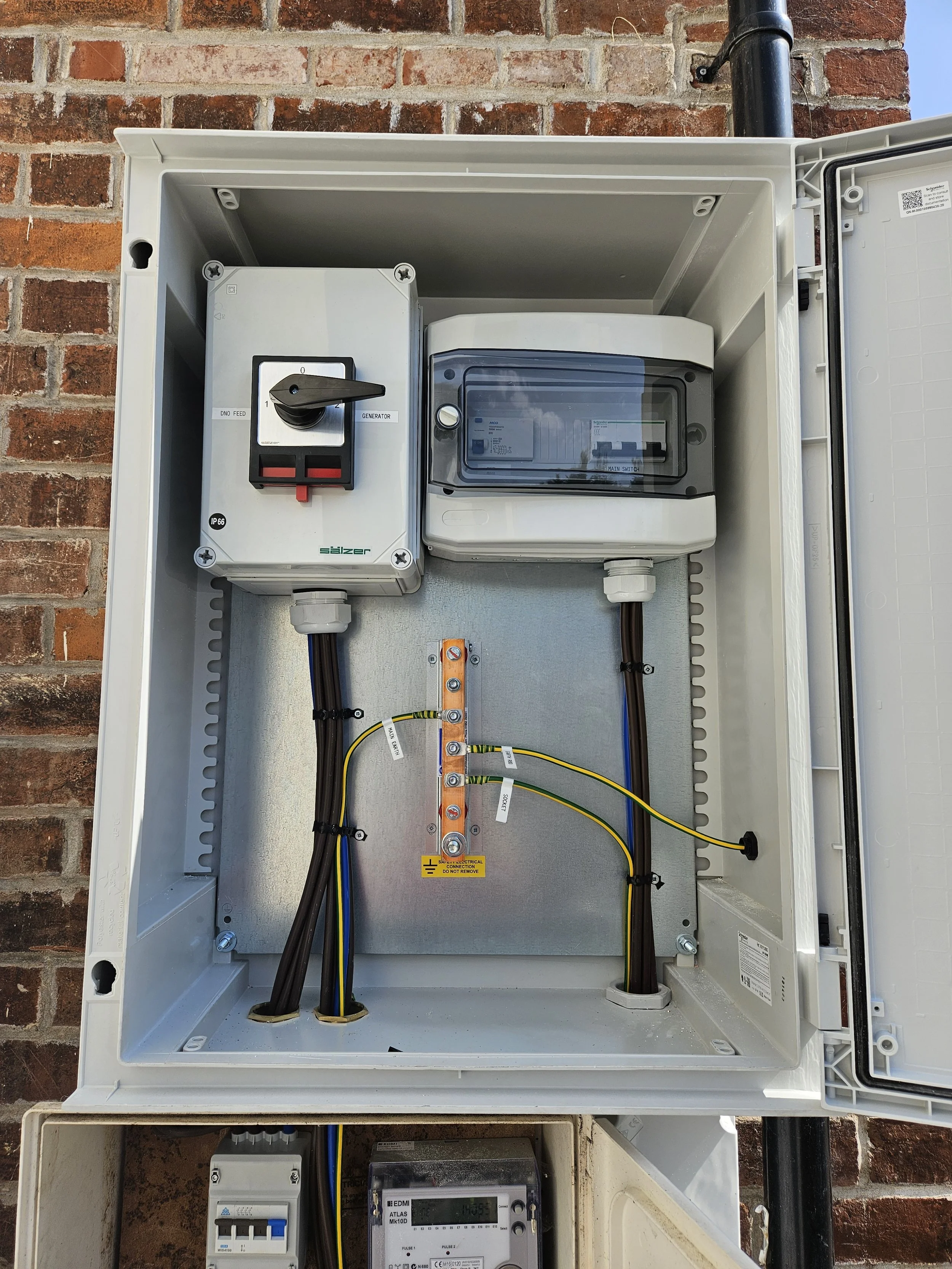 An electrical meter and circuit breaker inside a gray electrical box mounted on a brick wall.