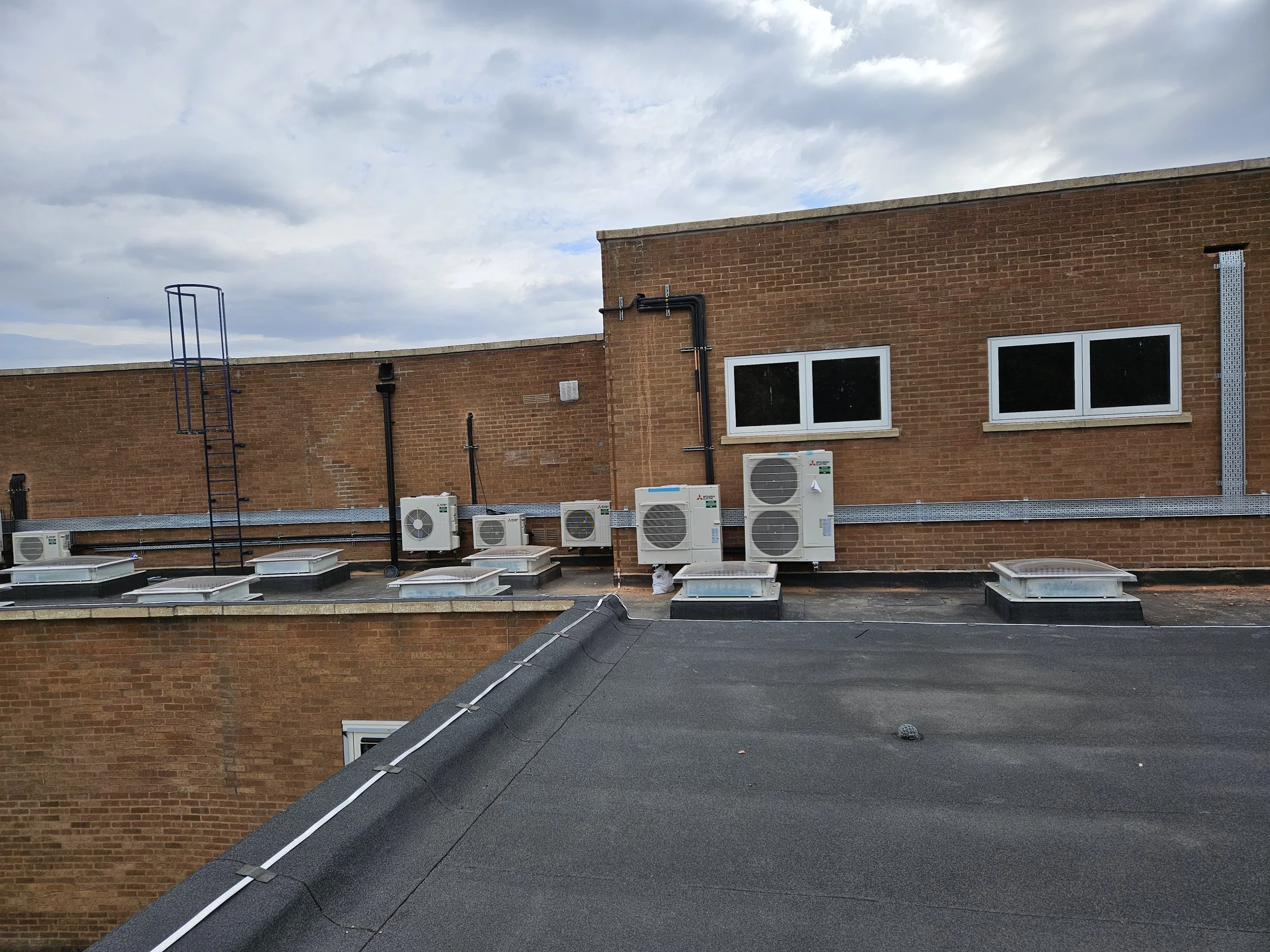 View of the rooftop of a brick building with several air conditioning units and vents, under a cloudy sky.