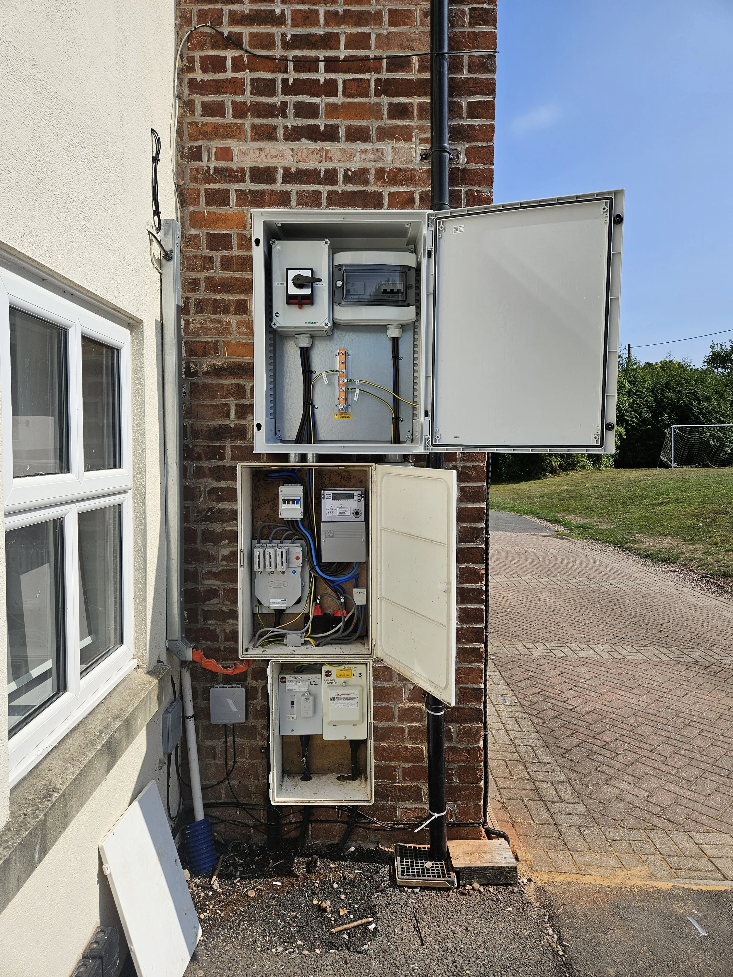 Outdoor electrical utility boxes mounted on a brick wall, with various switches, meters, and wiring.