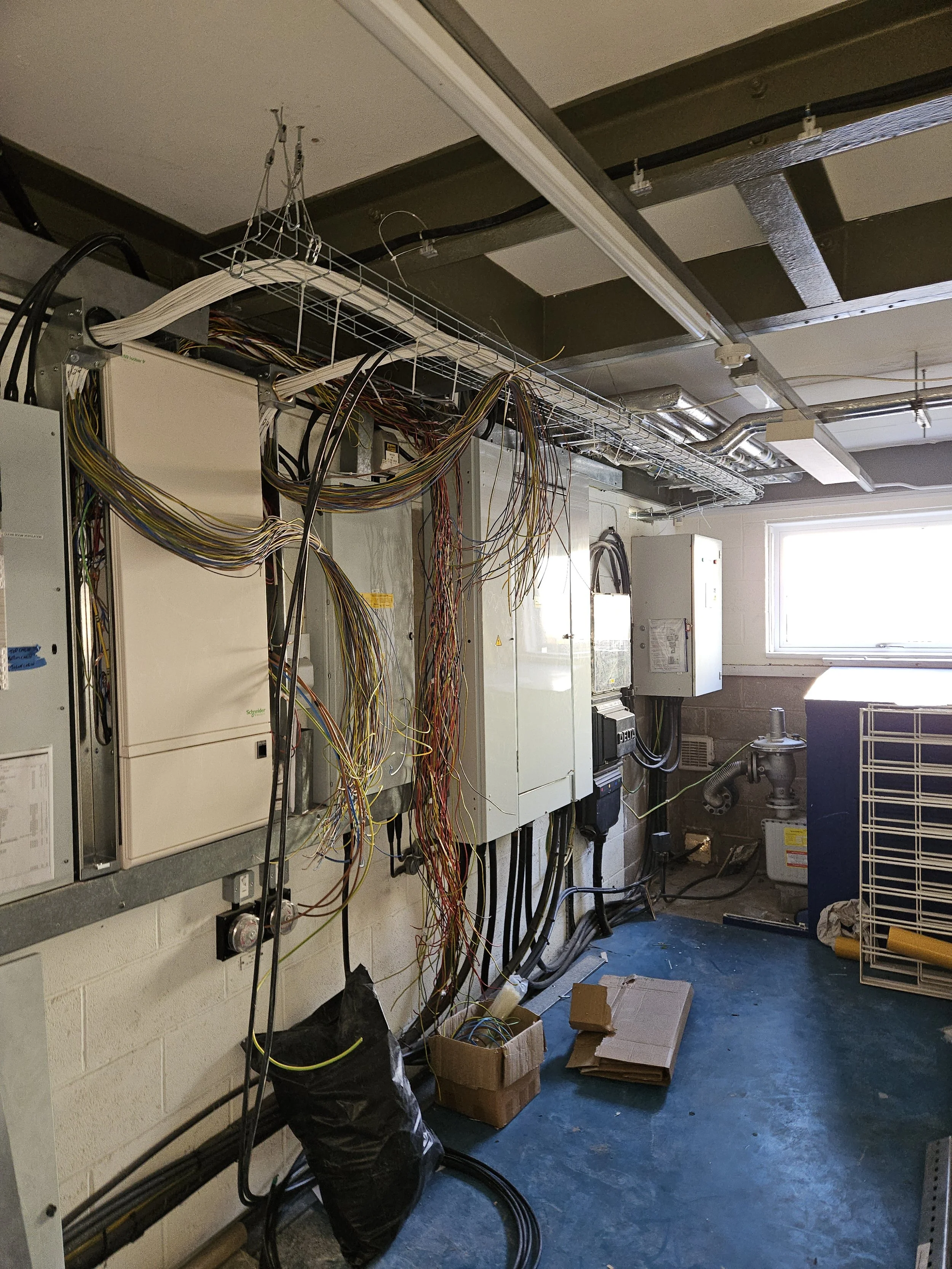 Electrical wiring and panels in an industrial or utility room with a window and some equipment.