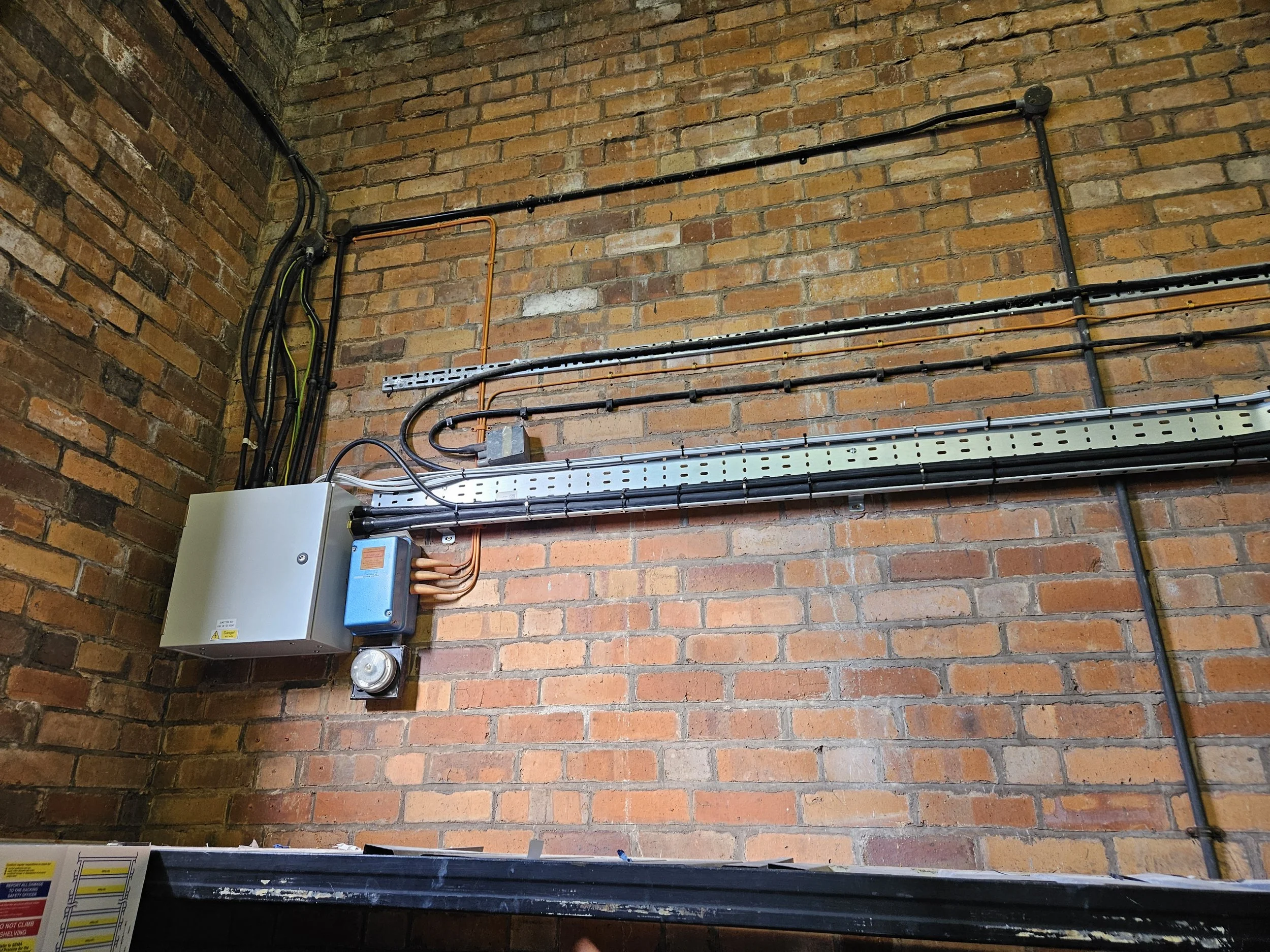 Electrical wiring and conduit on a brick wall, including electrical boxes and a metal cable tray.