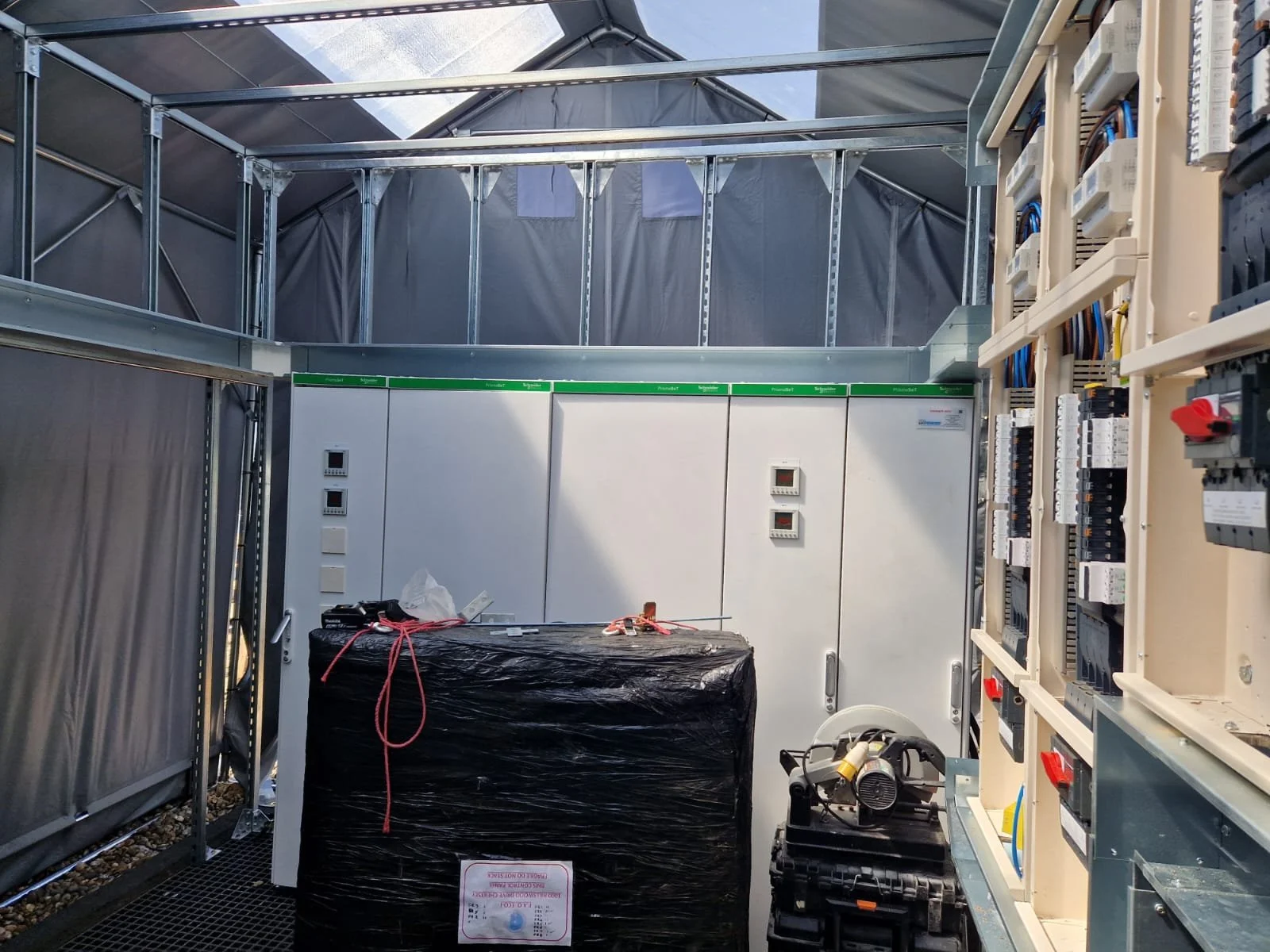 Interior view of an electrical or data control room with electrical panels, wiring, and equipment, in a tent-like structure with metal framing.