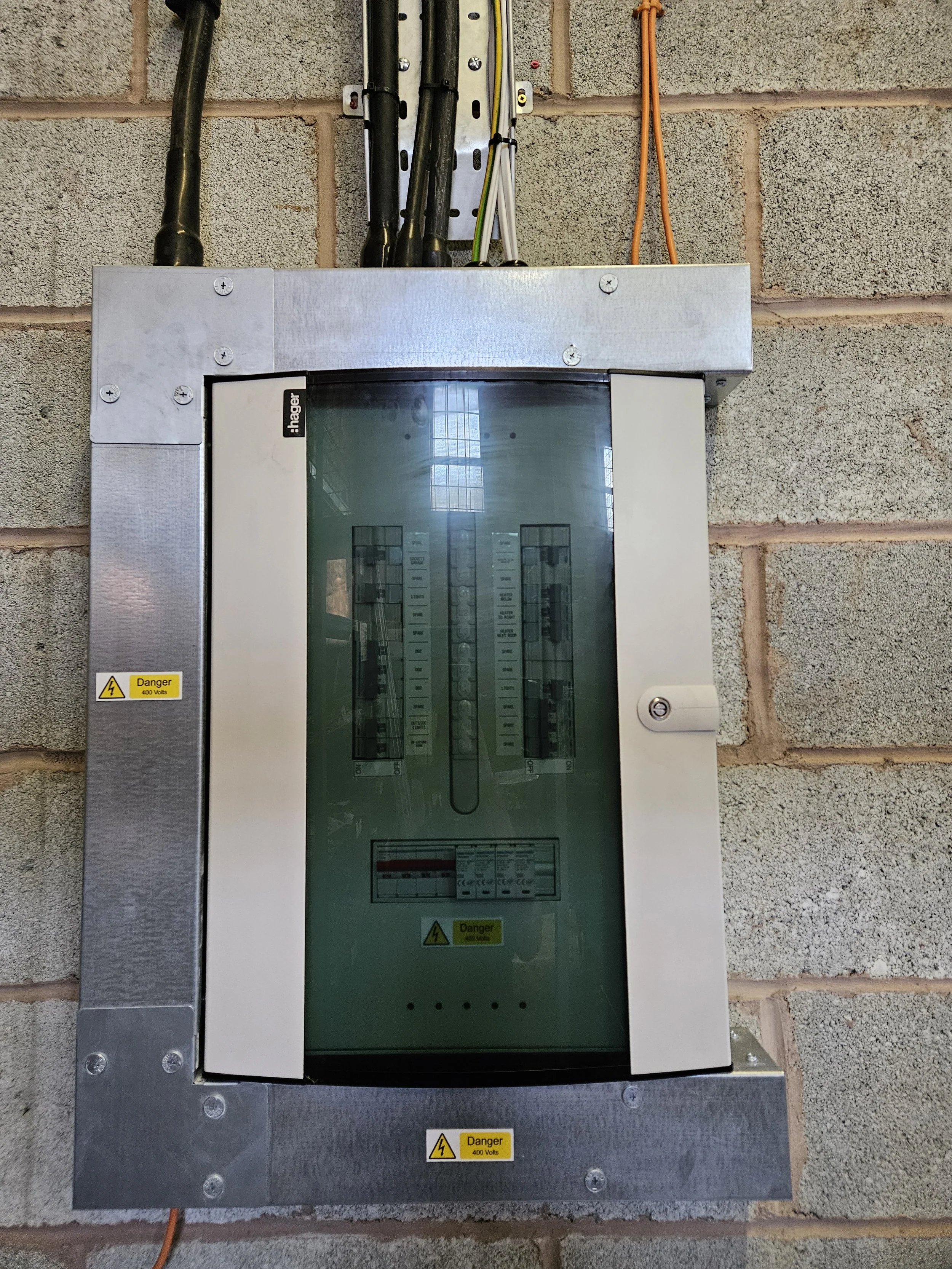 Electrical breaker box with a glass cover mounted on a brick wall, warning labels indicating danger of 400 volts.