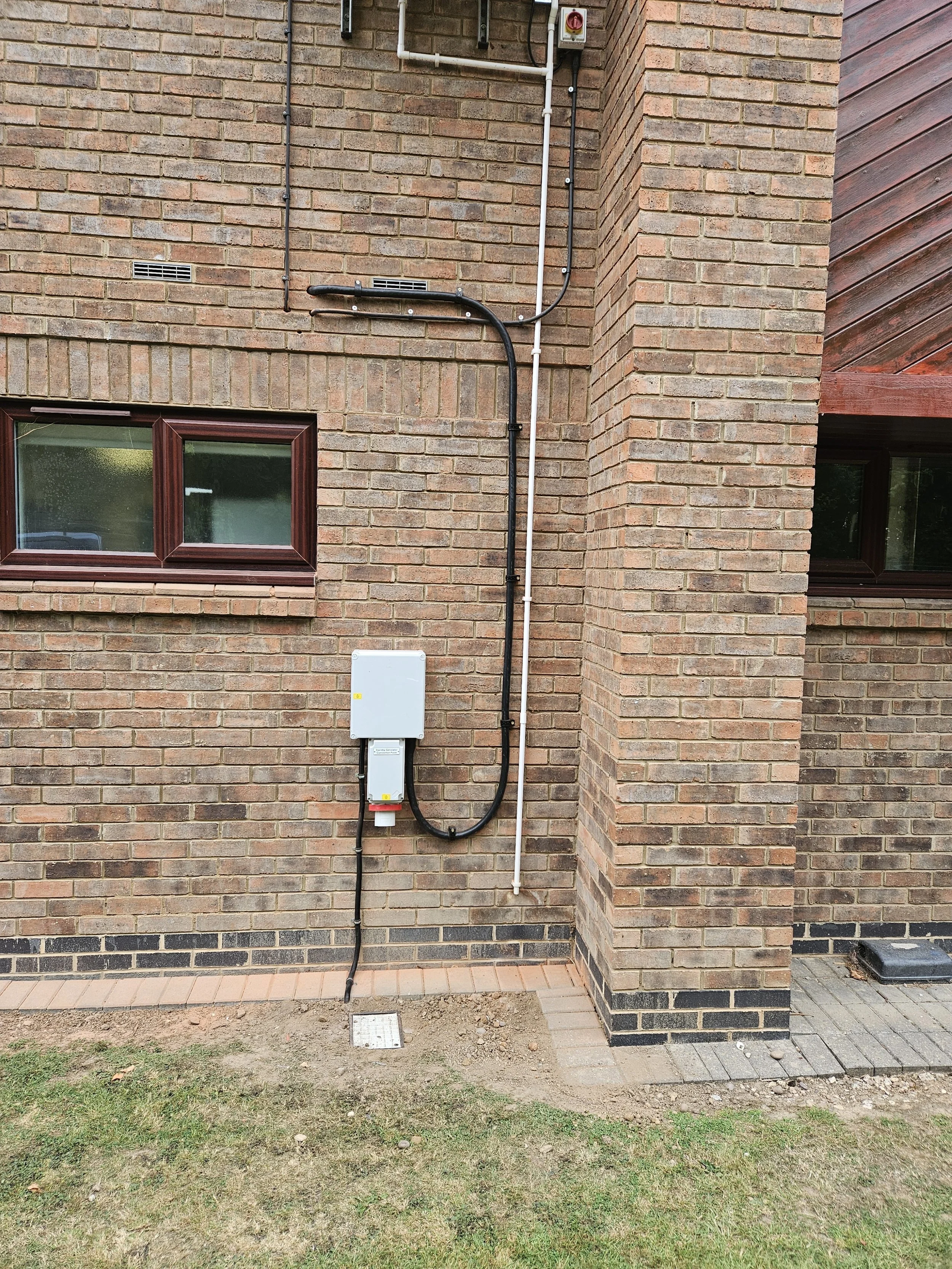 External view of a brick building showing utility meter and electrical wiring running vertically along the wall.