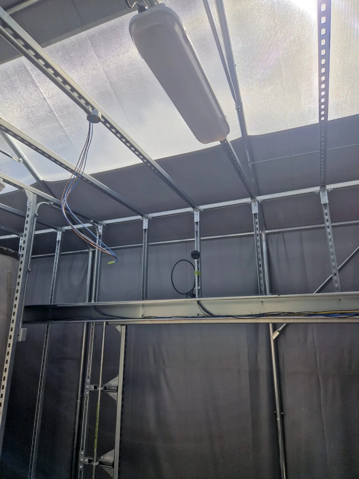 Inside of an unfinished building with metal framing and electrical wiring, ceiling, and a fluorescent light fixture.
