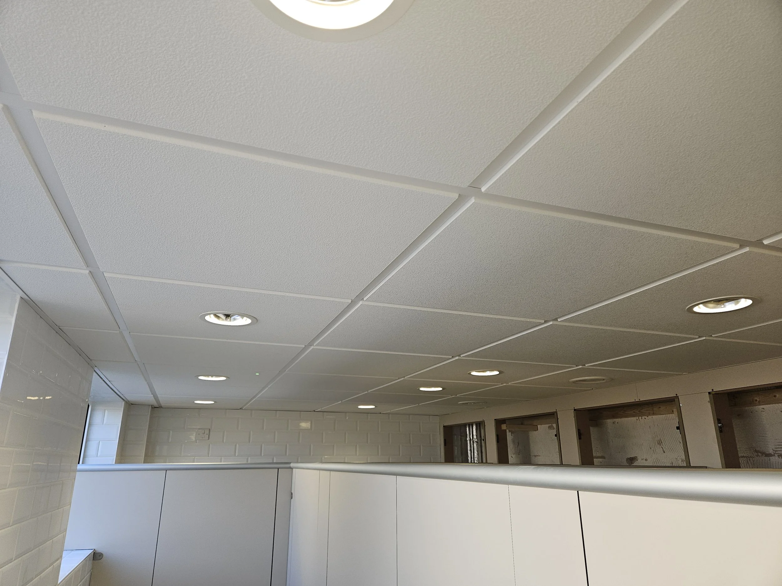 Ceiling with white textured acoustic tiles and recessed lighting in a modern interior space.