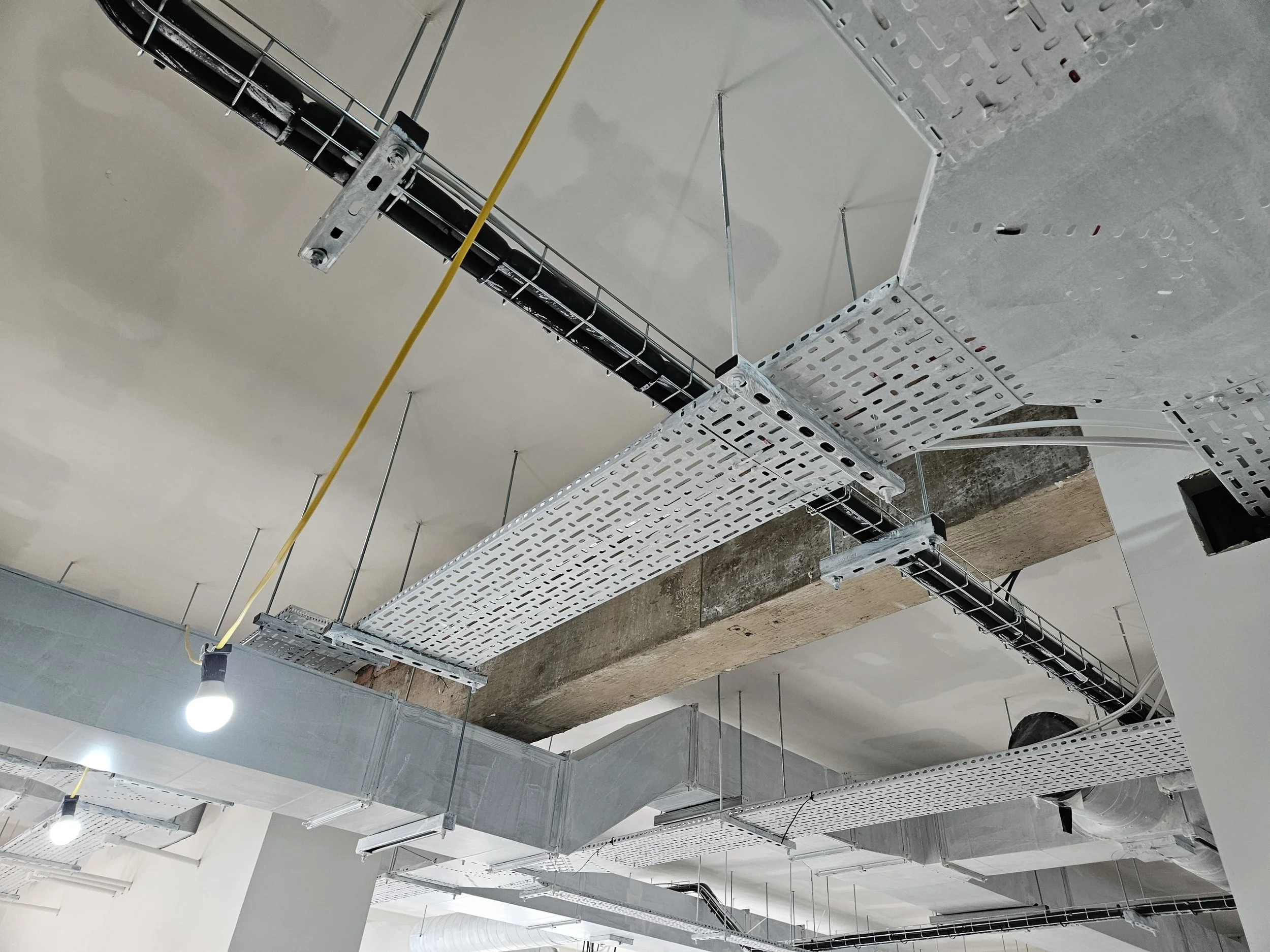 Ceiling construction with exposed metal ductwork, electrical wiring, and hanging light bulbs in a building under construction.