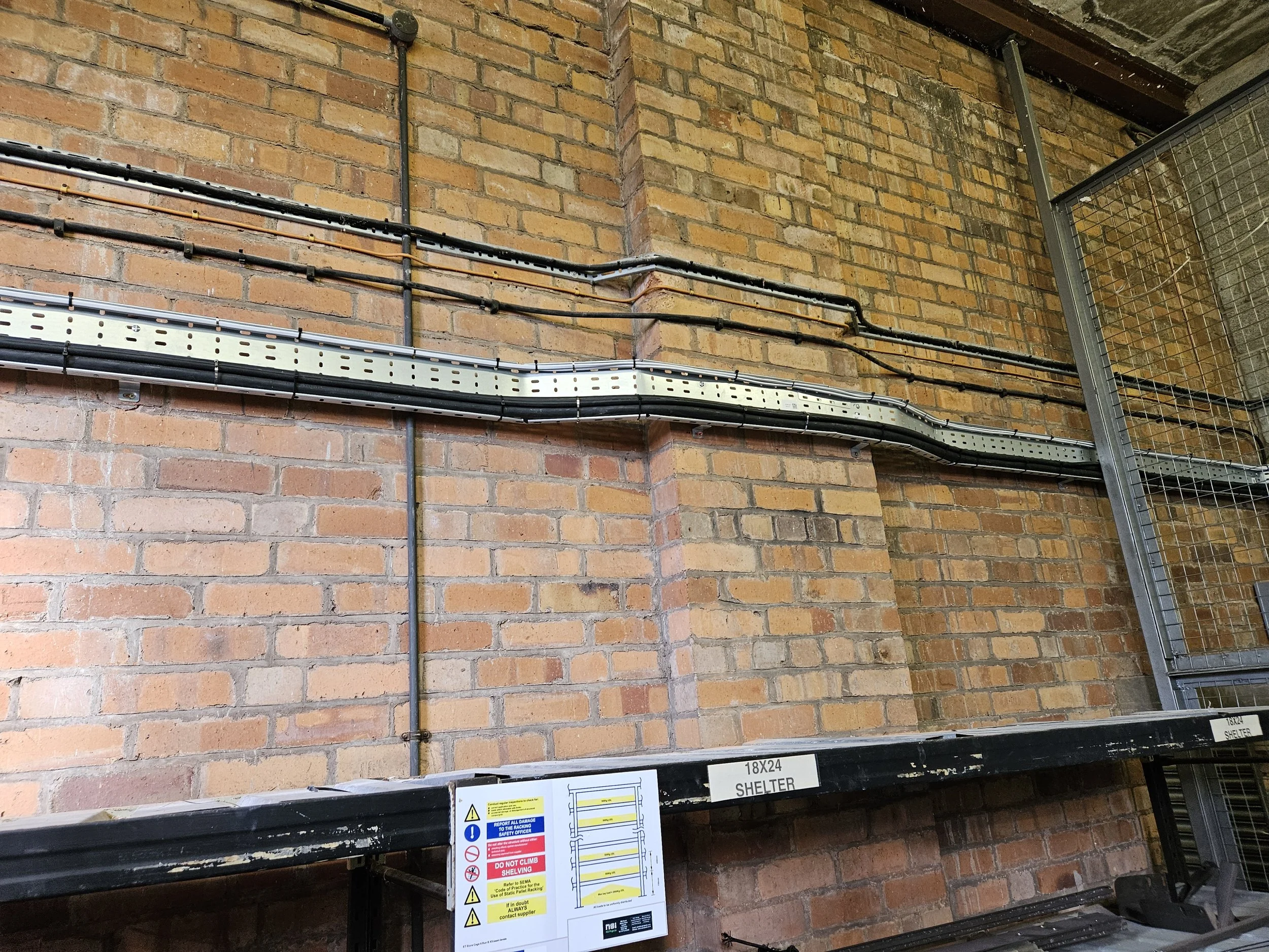 Electrical cables and conduits running along a brick wall and shelf in an industrial or warehouse setting.