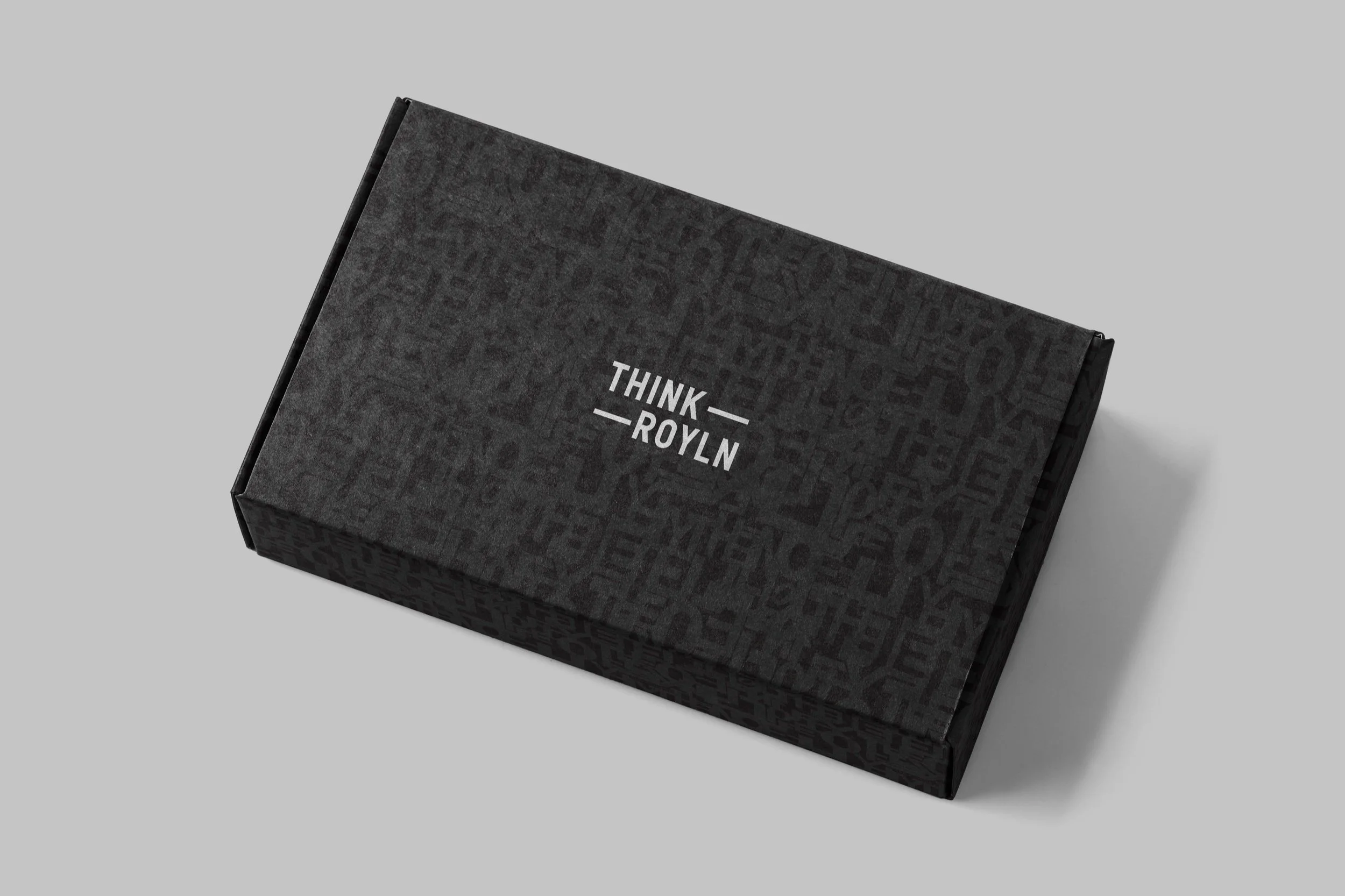Black rectangular box with the words "THINK ROYLN" in white, placed diagonally on a gray background.