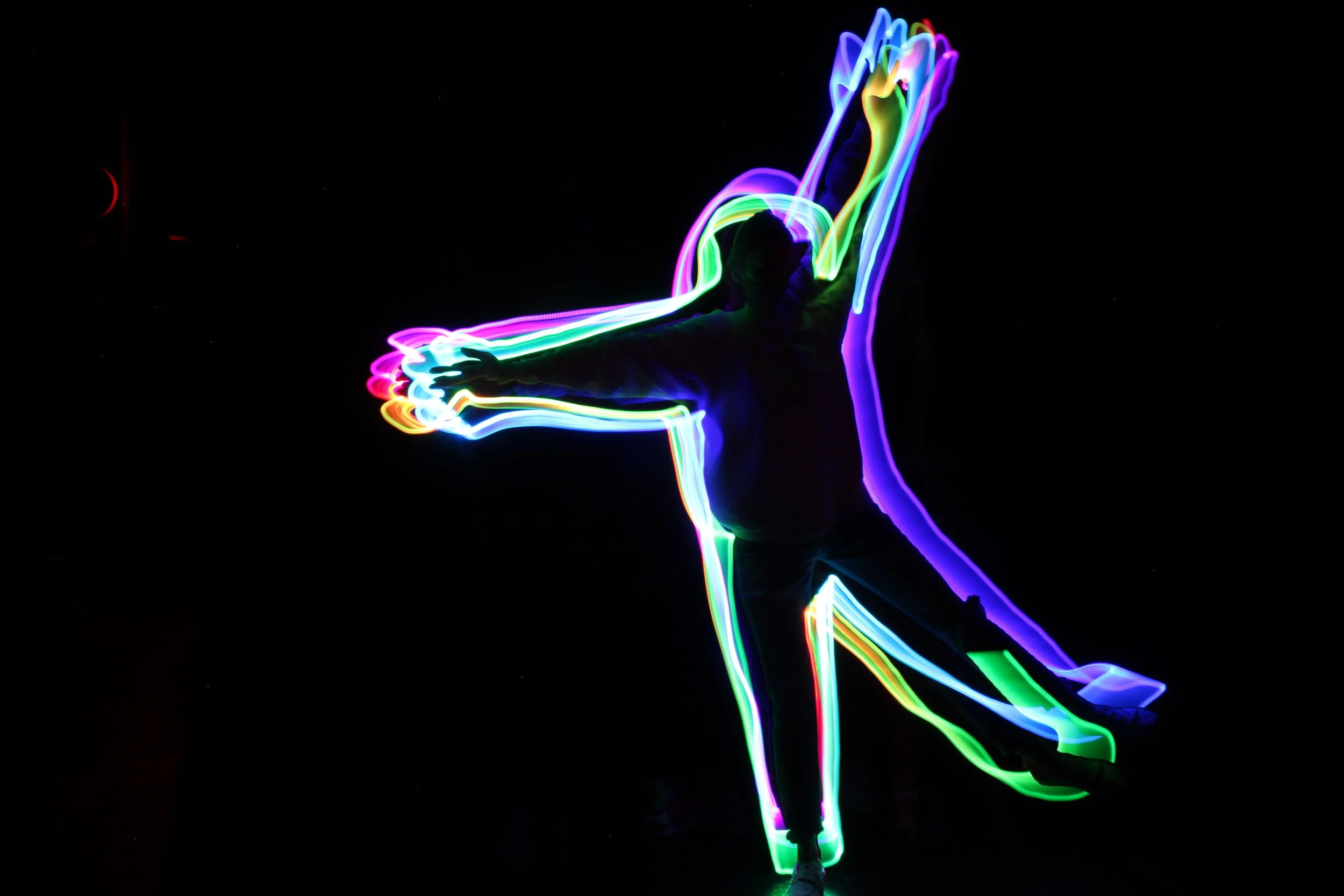 Person performing with colorful glow lights in the dark, creating streaks of neon colors.