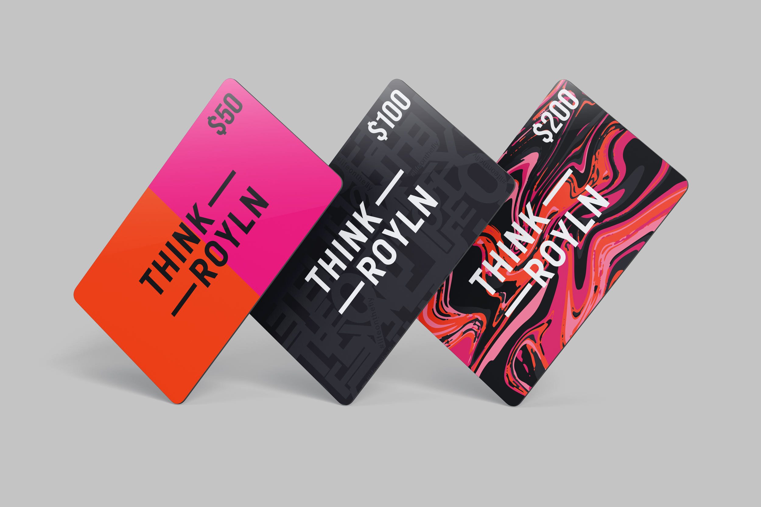 Three colorful gift cards with the phrase "Think Royln" on them, each with a different vibrant pattern and dollar amount: $50, $100, and $200, arranged in a diagonal line on a gray background.