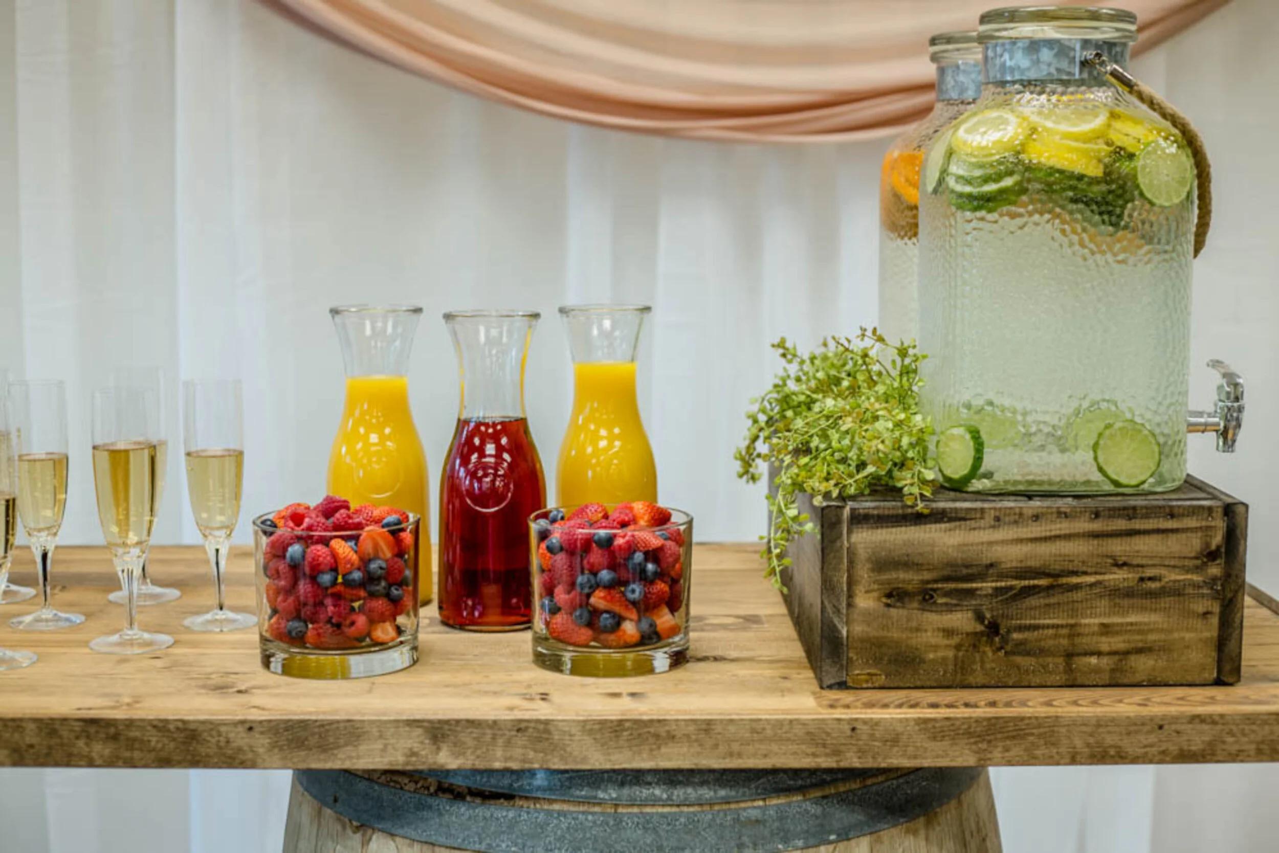 Two carafes of orange juice, one jug of cranberry juuic, and two glasses full of mixed berries sit on a wooden counter top.