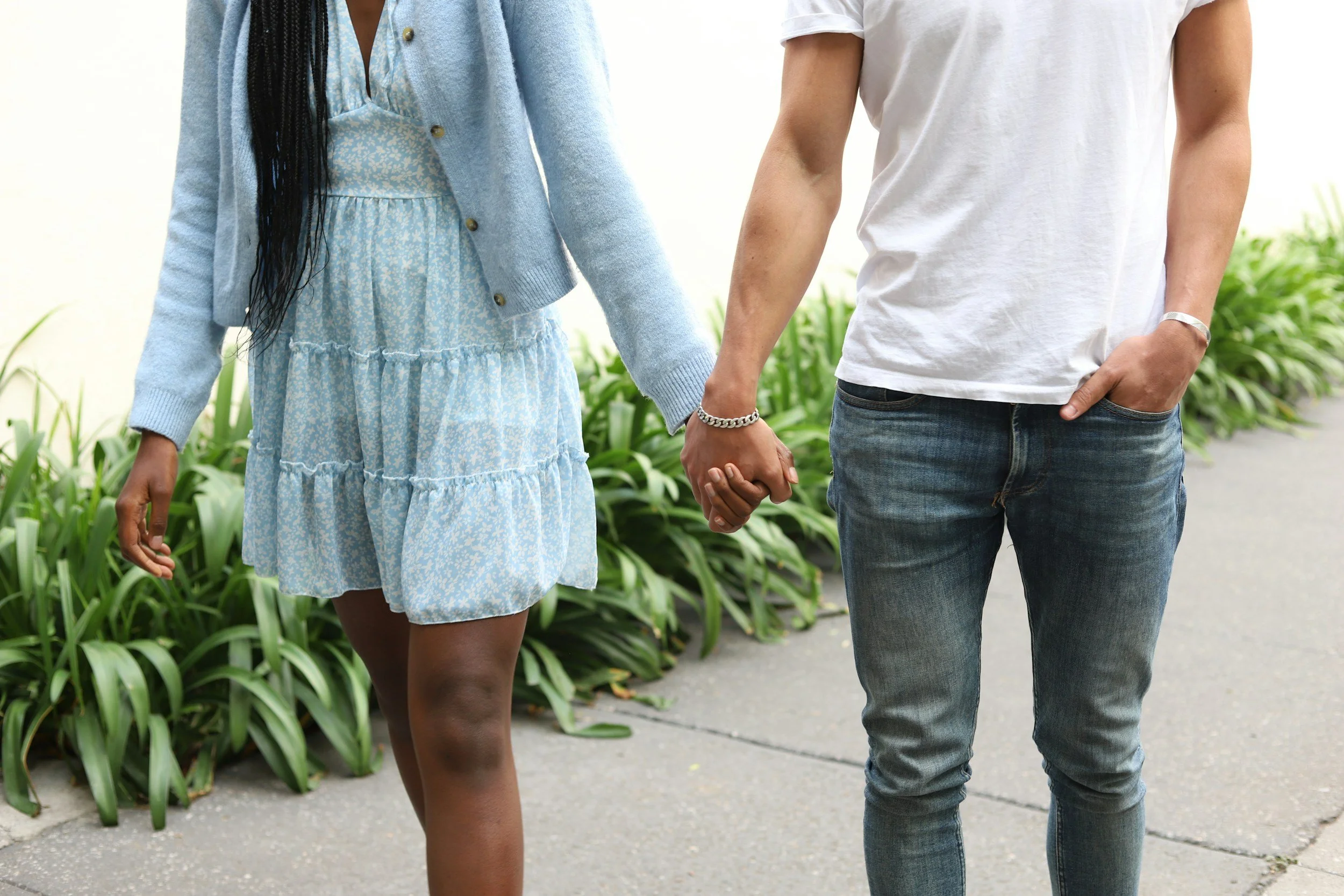 Couple walking hand in hand, woman in a blue dress and cardigan, man in a white shirt and jeans.