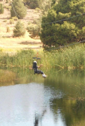 A person on a zipline over a peaceful mountain lake at summer camp