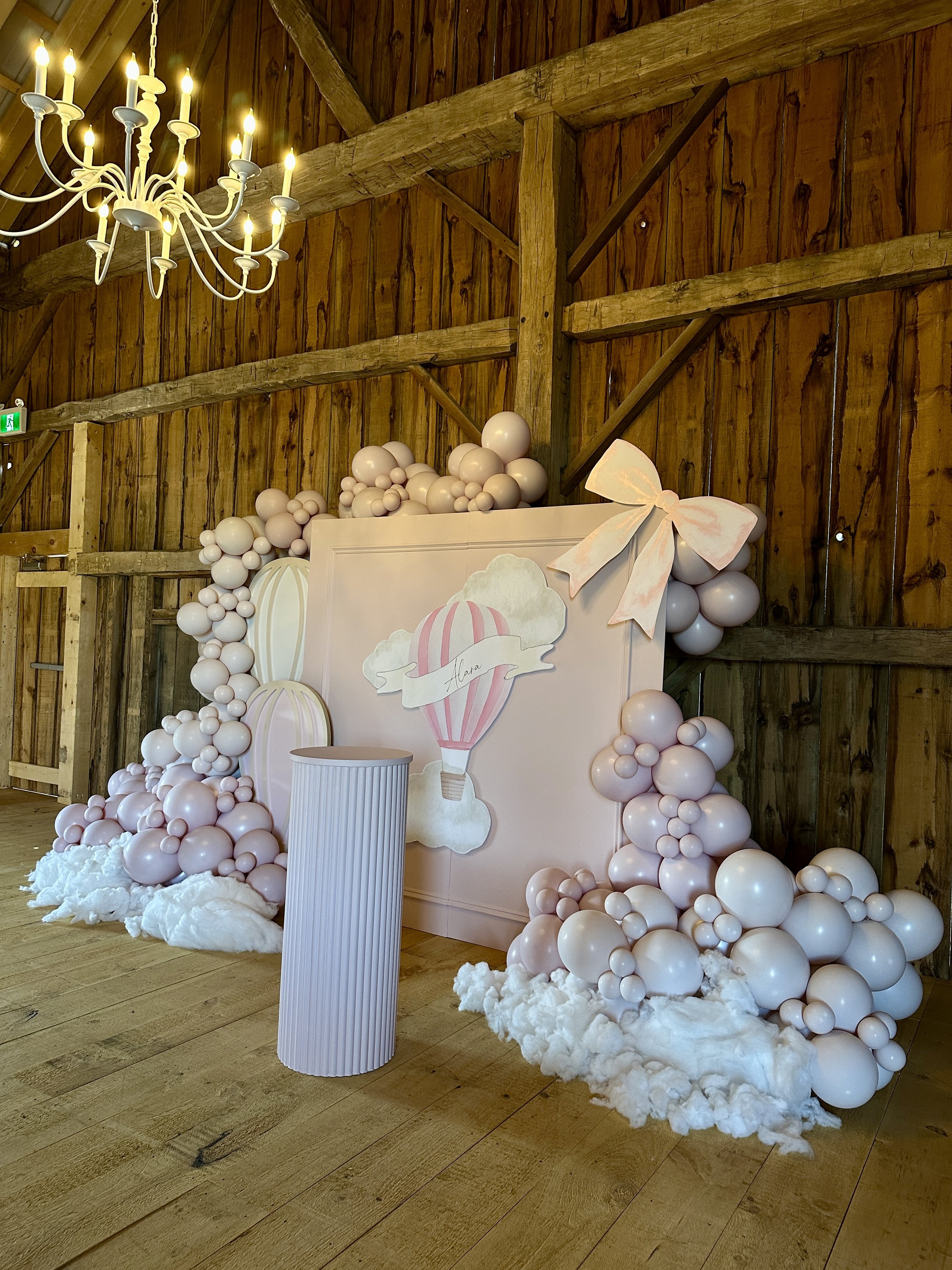 A styled event backdrop inside The Hummingbird barn in Erin, Ontario, featuring soft blush balloon installations, custom signage, and rustic wood beams for baby showers and intimate celebrations.
