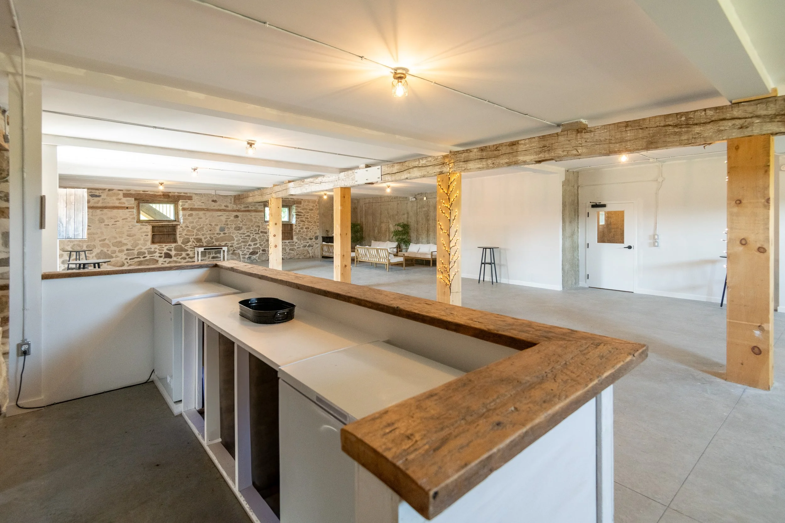 Spacious open-concept room with exposed stone and wood beams, minimal furniture, and some string lights on the support beams.
