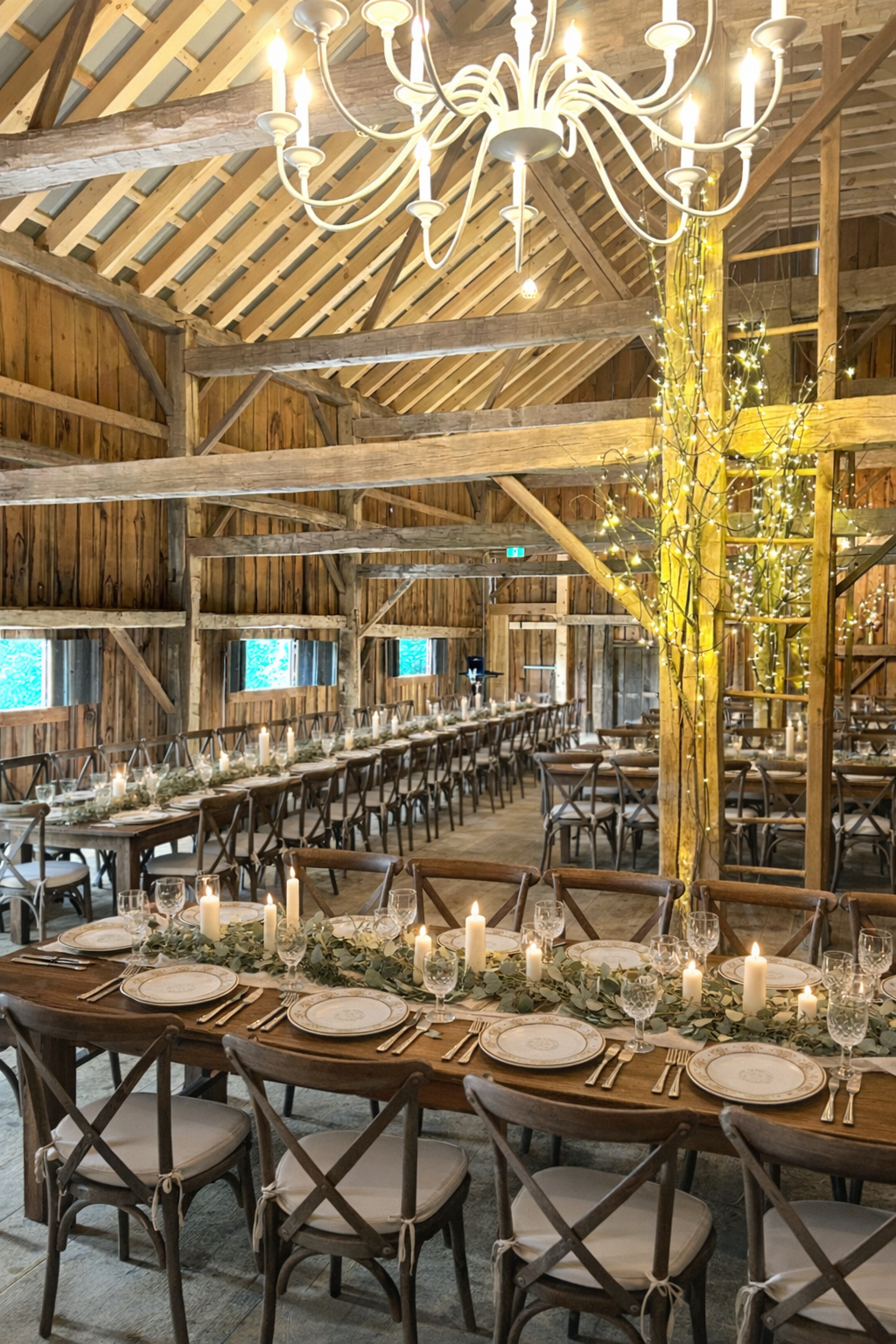 A refined barn wedding reception at The Hummingbird in Erin, Ontario, featuring long banquet tables set beneath a classic chandelier, original timber beams, and warm candlelight. Greenery garlands and heritage details create a timeless, elegant atmos
