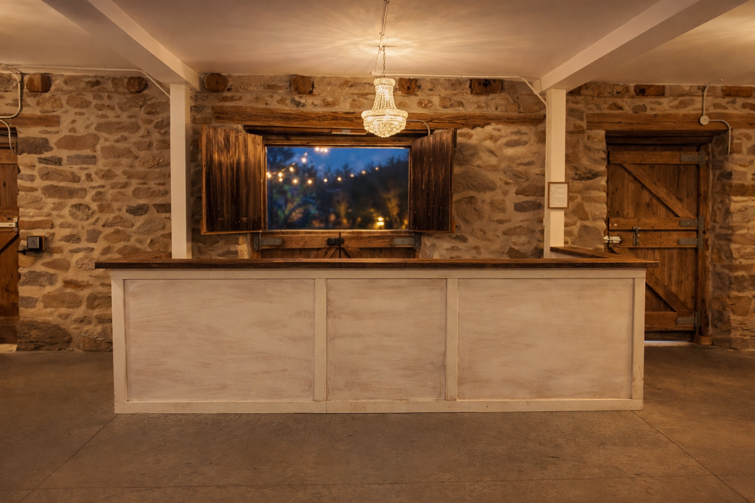 A refined bar space at The Hummingbird in Erin, Ontario, featuring exposed stone walls, a handcrafted wood bar, and soft chandelier lighting. Designed to complement the character of the historic barn, the bar serves as a natural gathering point durin