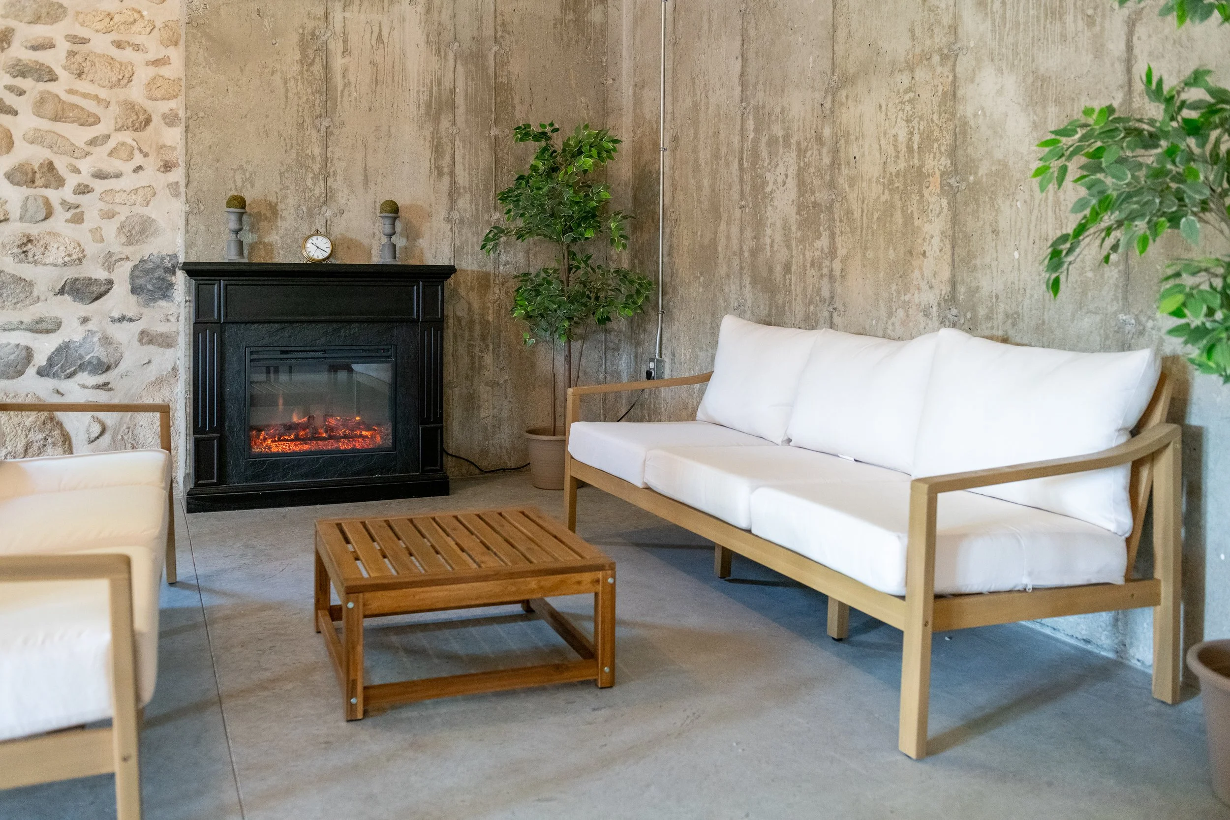 Living room with a black fireplace, white sofas, a wooden coffee table, potted plants, and a stone wall.