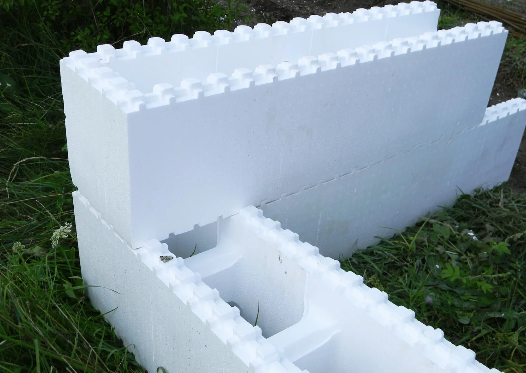 White polystyrene foam blocks with interlocking edges, stacked outdoors on grass, possibly for construction or insulation.