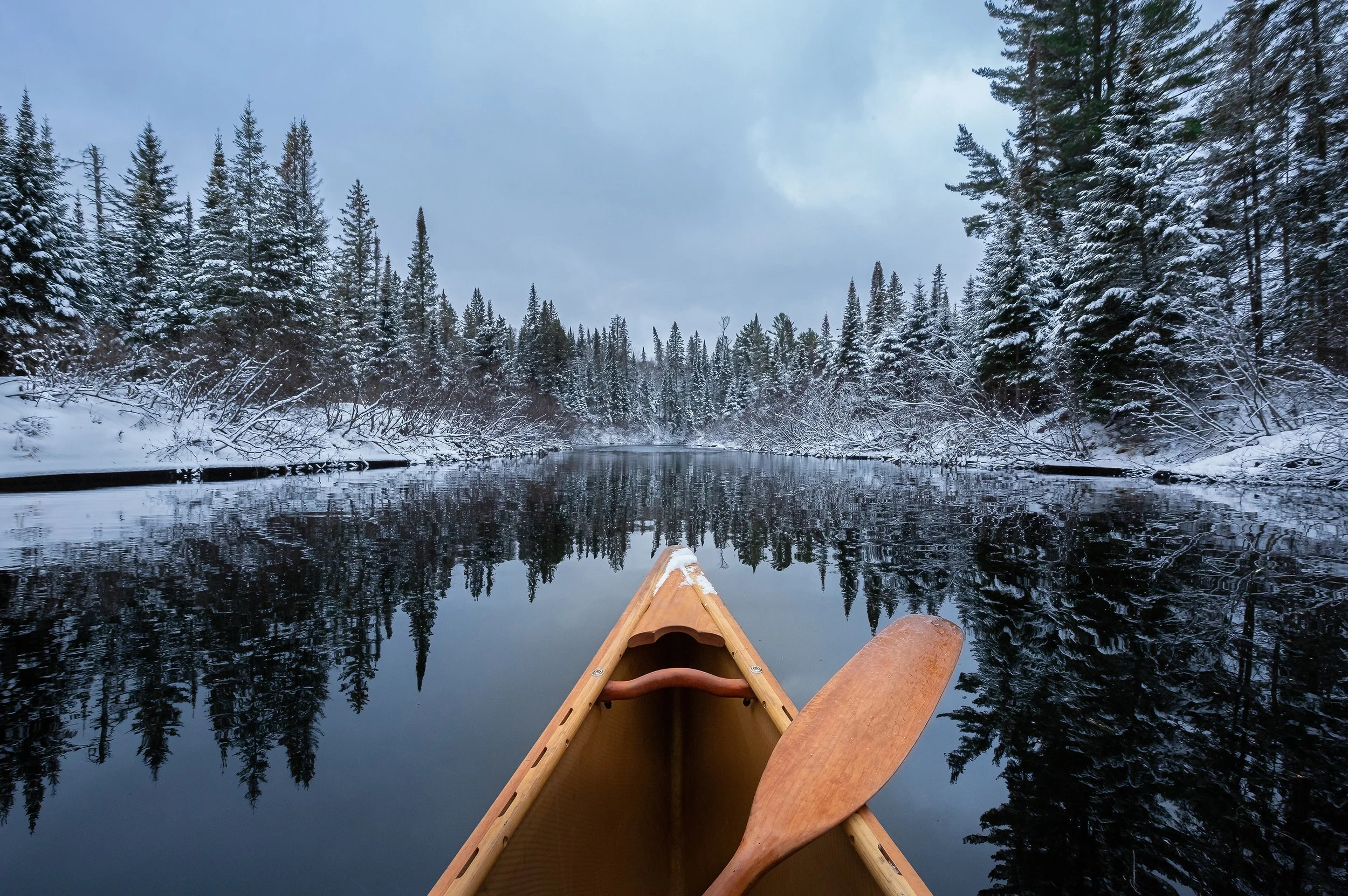 Front of a canoe in a Winter landscape with still water
