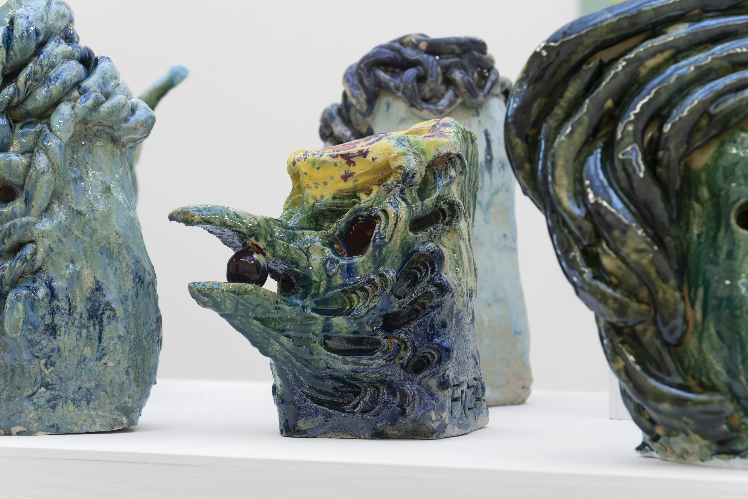 Colorful ceramic sculptures resembling abstract human faces and hands, displayed on a white surface. Frederik Næblerød Time to Move exhibition at  Horsens Art museum Kunstmuseum, Denmark.