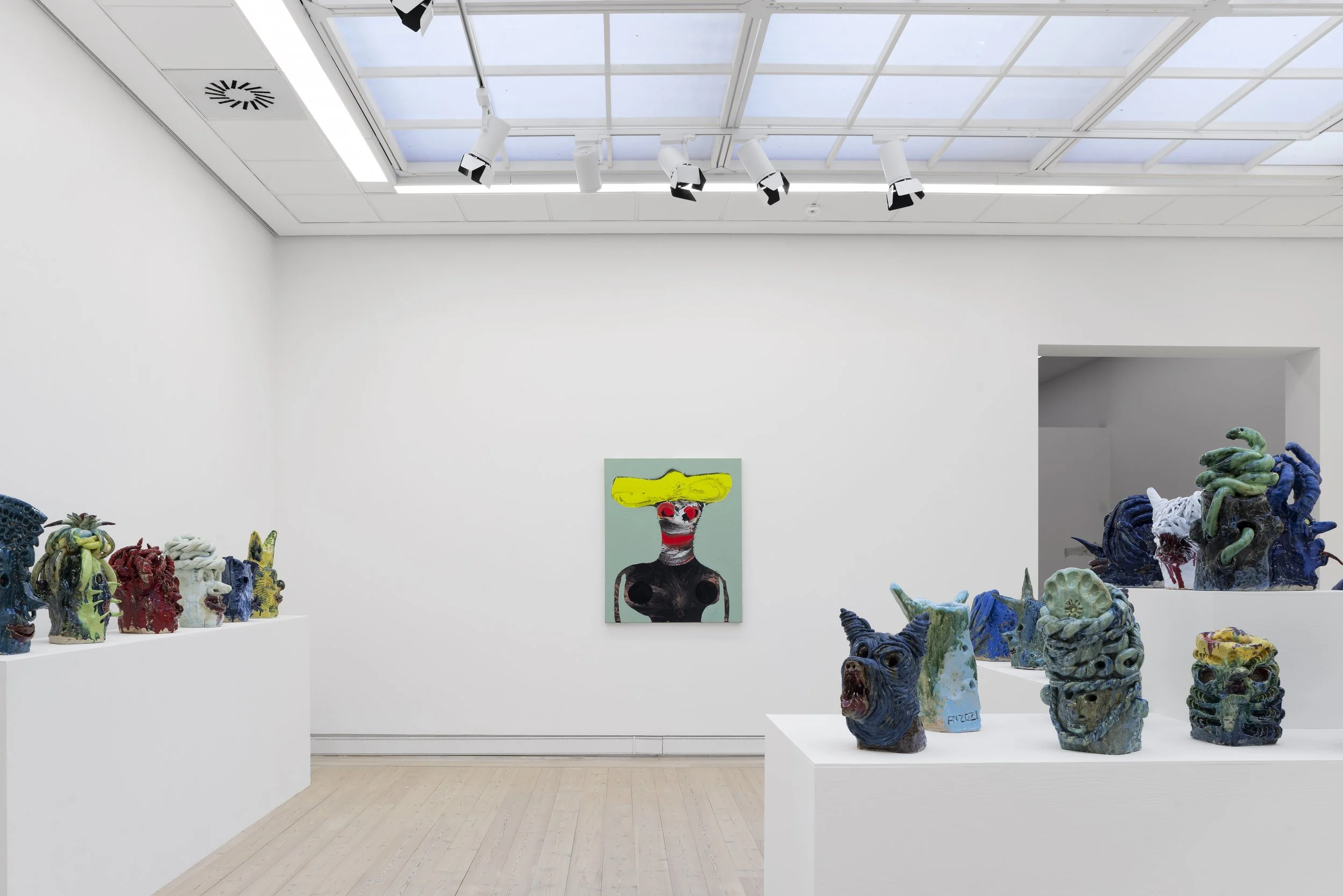 Art exhibit in a gallery with colorful ceramic sculptures of various creatures and a modern painting of a figure with a yellow hat and red facial features on the wall. Frederik Næblerød Time to Move exhibition at  Horsens Art museum Kunstmuseum, Denm