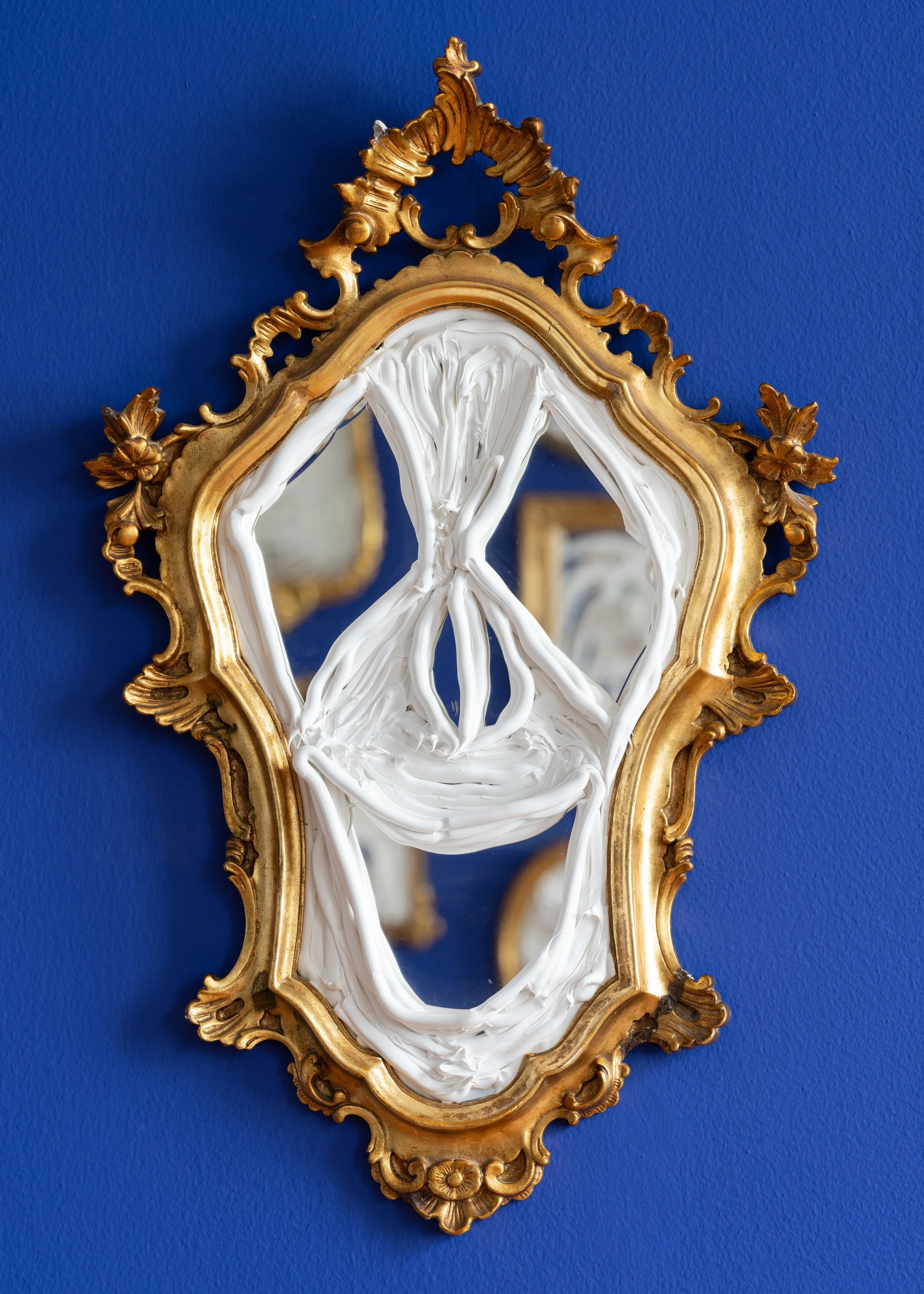 An ornate gold-framed mirror with white paint smeared over the glass, partially obscuring the reflection, mounted on a dark blue wall. Frederik Næblerød exhibition at Gl. Holtegaard, Denmark.