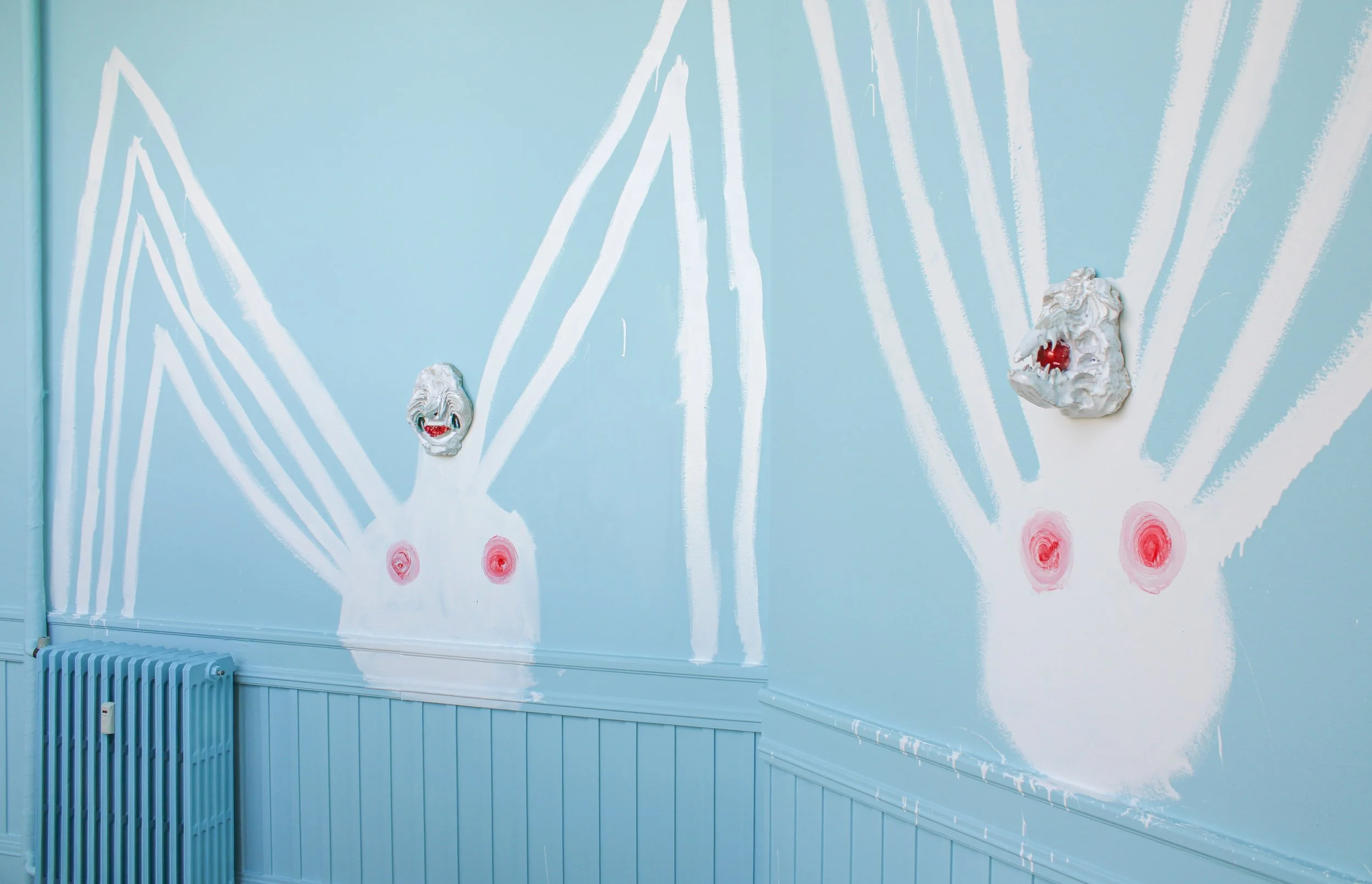 Blue wall with white abstract lines and two distorted masks with red mouths and pink circular patterns below, resembling exaggerated human features. Frederik Næblerød exhibition at Alice Folker Gallery, Denmark.