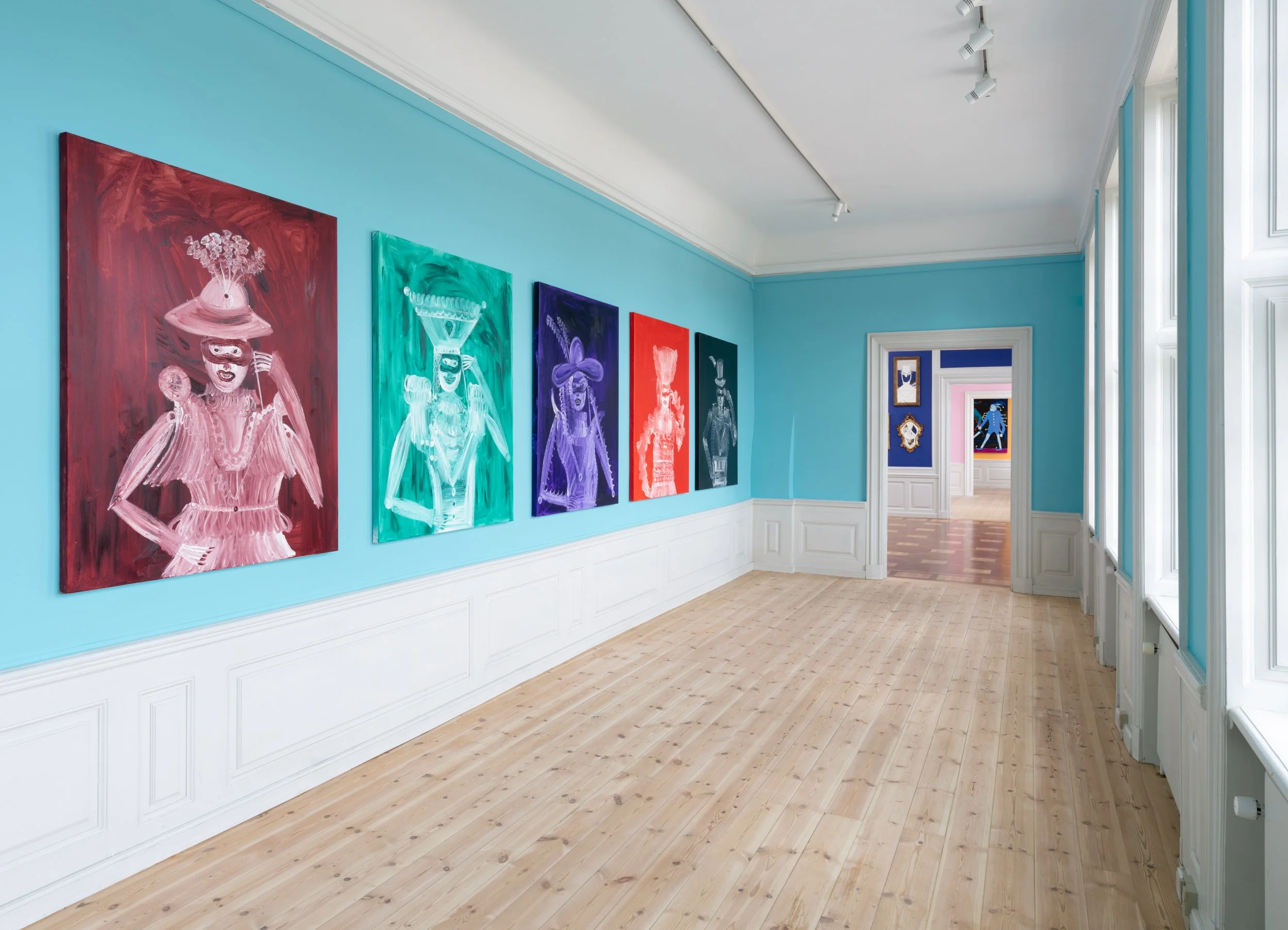 An art gallery with painted portraits on a light blue wall, featuring colorful and abstract depictions of women, with large windows on the right and a doorway leading to more artwork in the background. Frederik Næblerød exhibition at Gl. Holtegaard, 