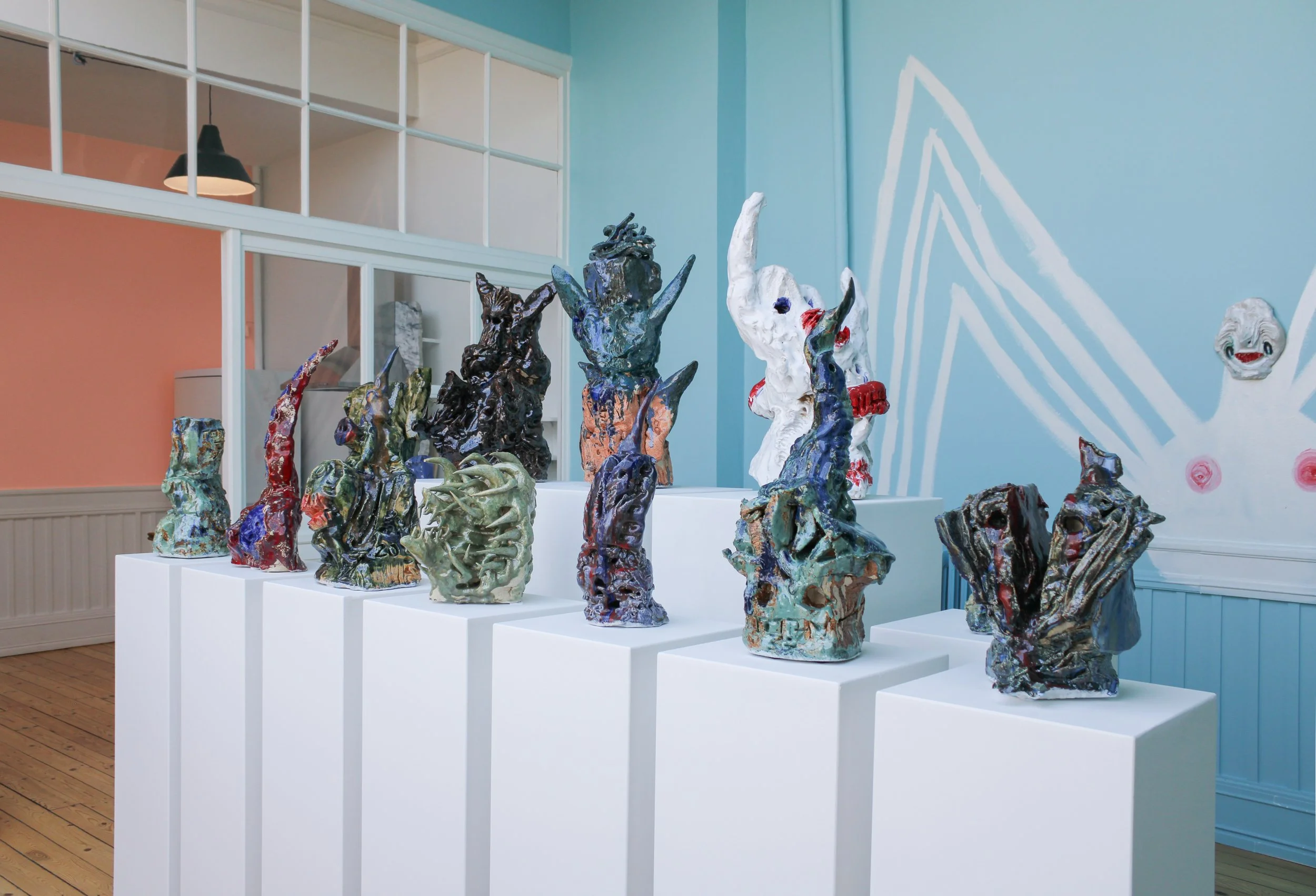 Ceramic sculpture art exhibit featuring multiple abstract and figurative ceramic sculptures displayed on white pedestals in a gallery with pastel blue walls. Frederik Næblerød exhibition at Alice Folker Gallery, Denmark.