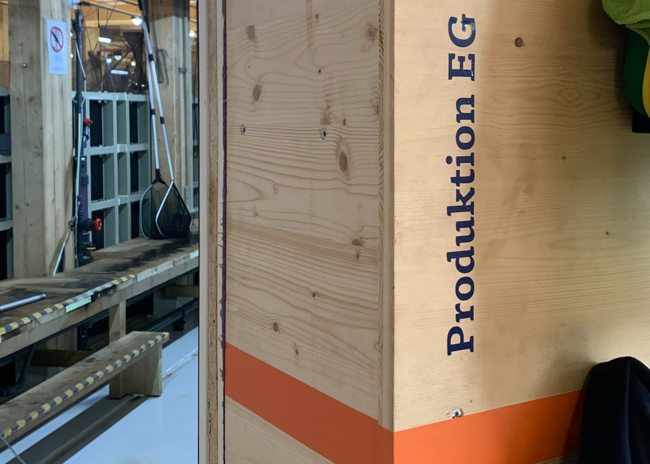 Holzbox mit der Aufschrift 'Produktionsreg' und Werkstatt im Hintergrund.