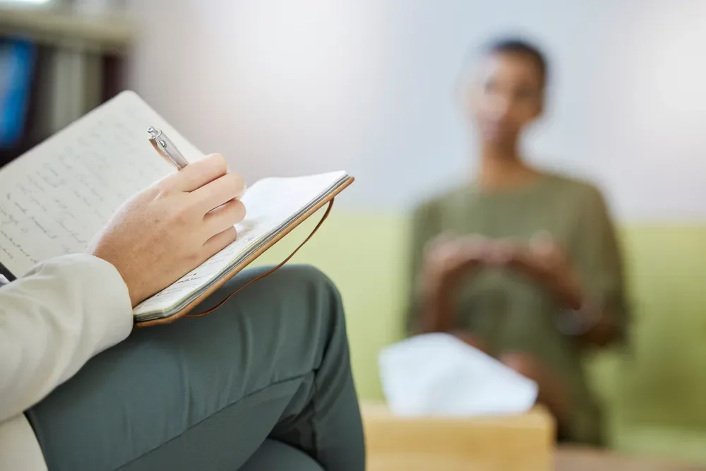 Therapist taking notes while speaking with a client during a mental health therapy session in Singapore.